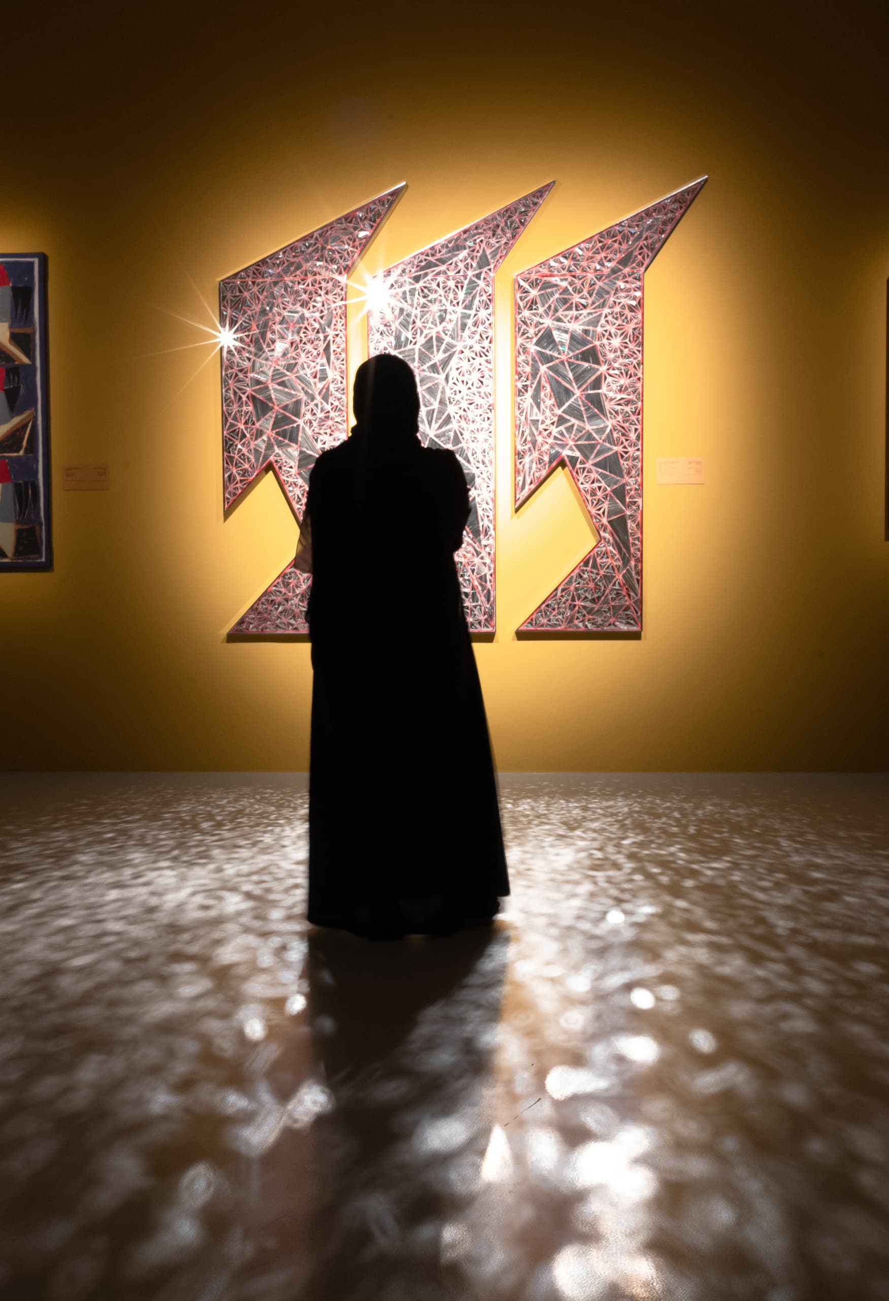 Dunkler Raum mit akzentuierten Bilder an der Wand, Frau steht davor und betrachtet Kunst. 