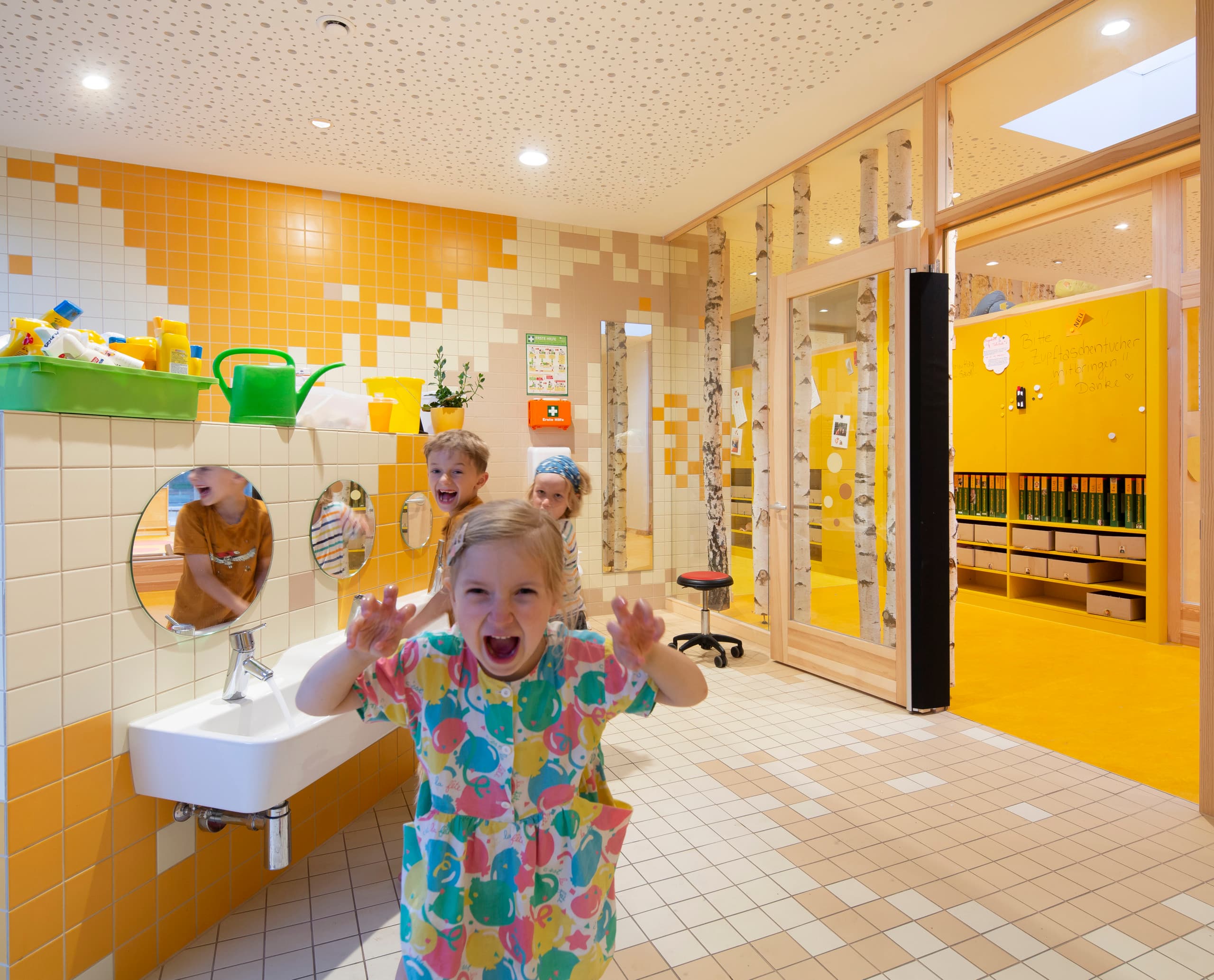 Kinder spielen im hellen Waschraum der Rappelkiste Kita, beleuchtet mit ERCO LED-Leuchten.