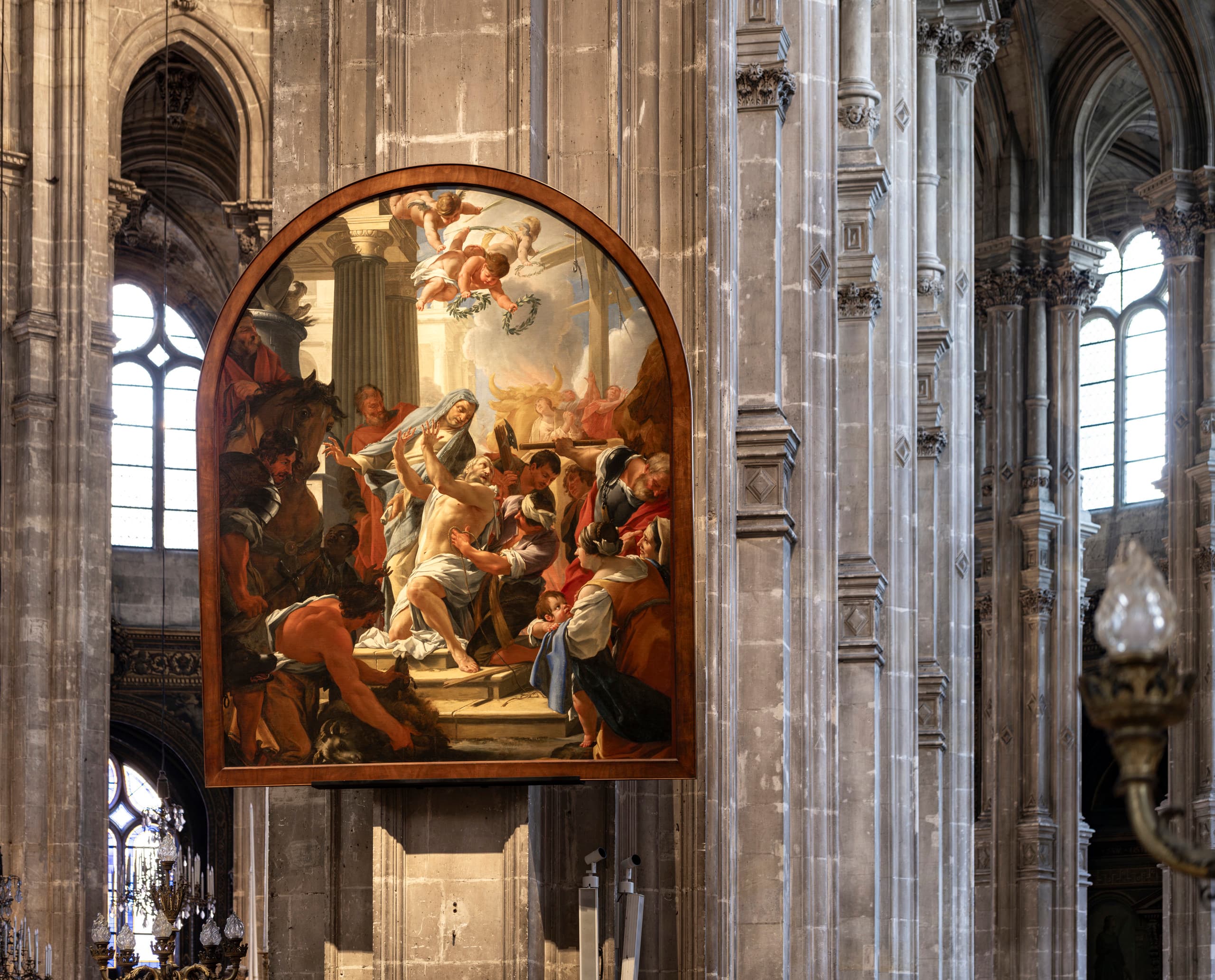 Ein großes, gerahmtes Gemälde, das eine dramatische biblische Szene darstellt und an einer Steinsäule in einer prächtigen gotischen Kirche hängt. Das farbenfrohe Kunstwerk zeigt mehrere Figuren in dynamischen Posen vor einem architektonischen Hintergrund. Das Gemälde wird von den hohen Steinbögen, den Rippengewölben und den Buntglasfenstern im Inneren der Kirche eingerahmt.
