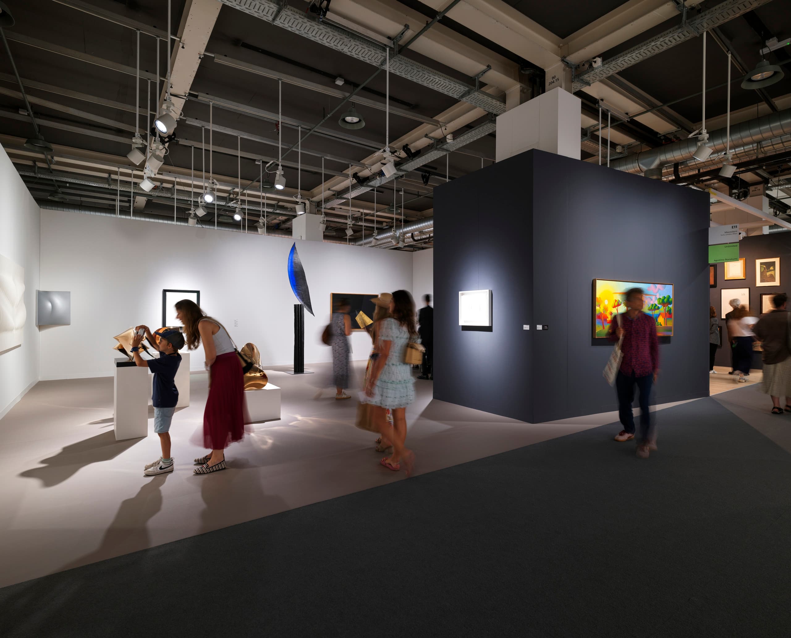 Stand auf der Art Basel mit weißer und schwarzer Wand, Kind macht Foto von einem Bild.