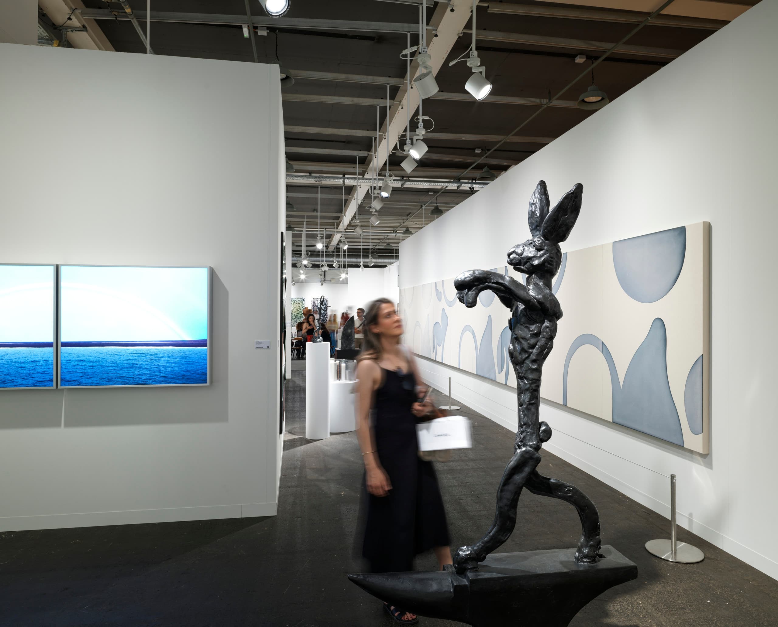 Frau guckt sich auf Messestand der Art Basel eine Hasen-Skulptur an.