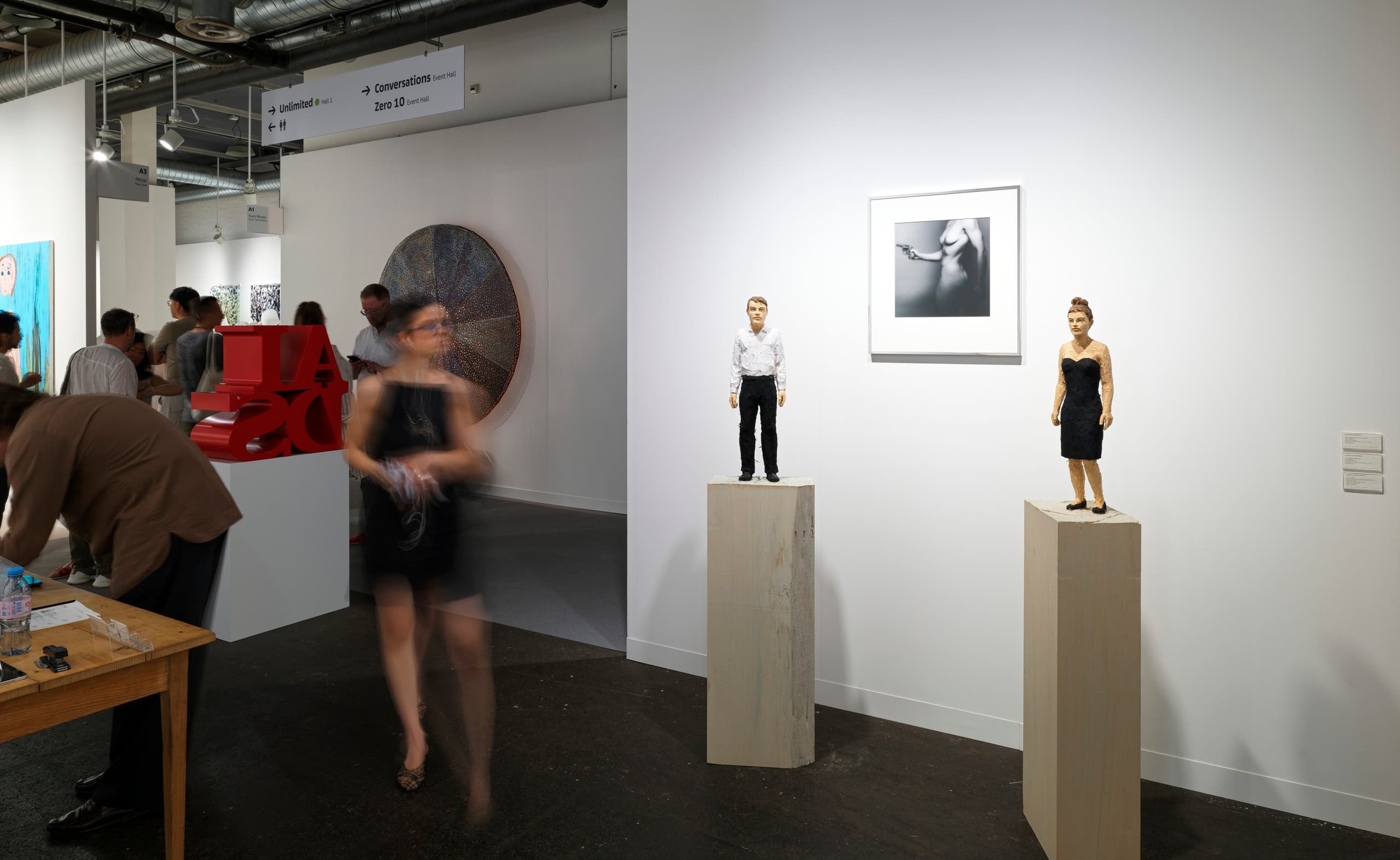 Besucherin neben zwei Skulpturen - Mann und Frau - auf Stand der Art Basel. 