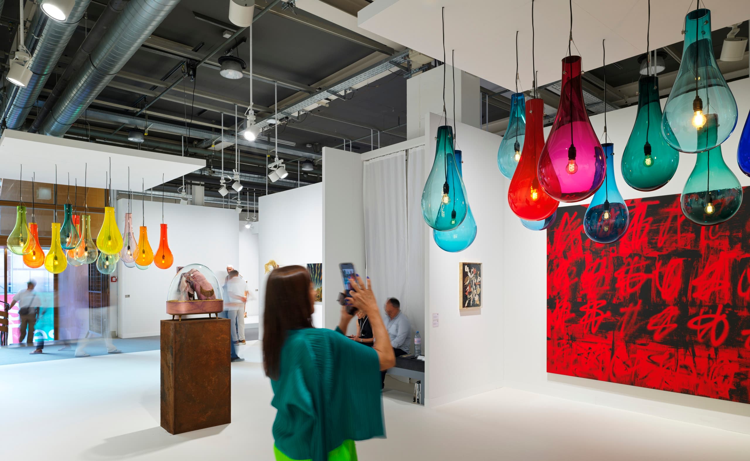 Frau macht ein Foto von einer Kunstinstallation aus bunten Glaslampen auf der Messe Art Basel.