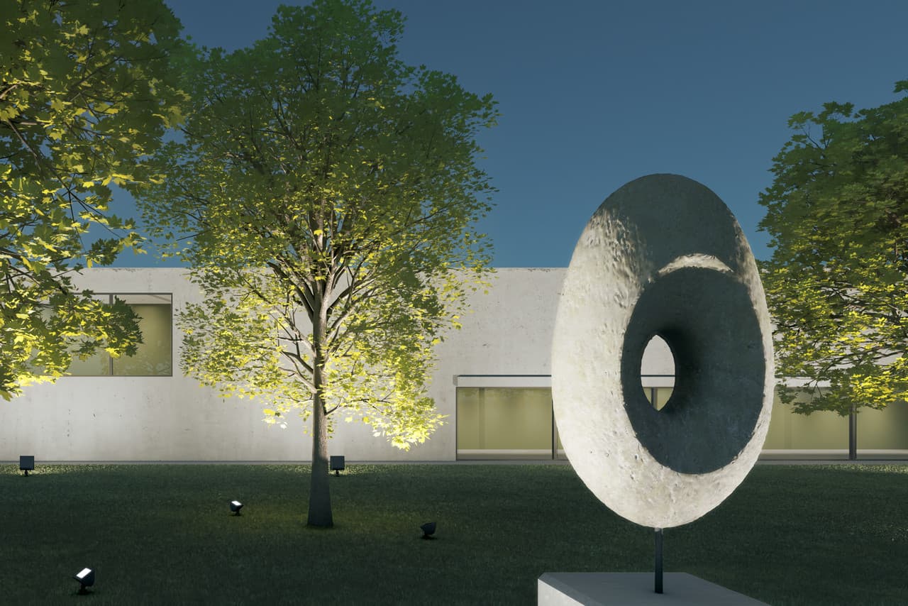 Beleuchtete Skulptur im Vordergrund, Bäume im Mittelgrund und Fassade im Hintergrund.