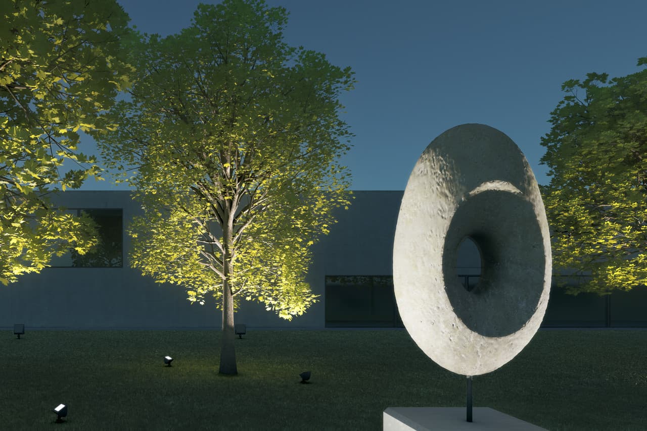 Beleuchtete Skulptur im Vordergrund, Bäume im Mittelgrund und Fassade im Hintergrund.