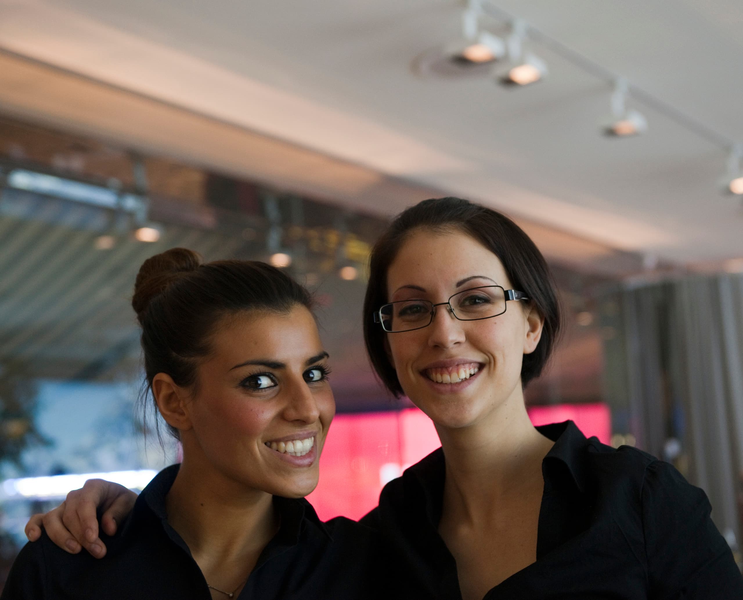Zwei lächelnde Frauen unter ERCO Light Board Strahlern in der Swiss Corner Bar, Mailand.