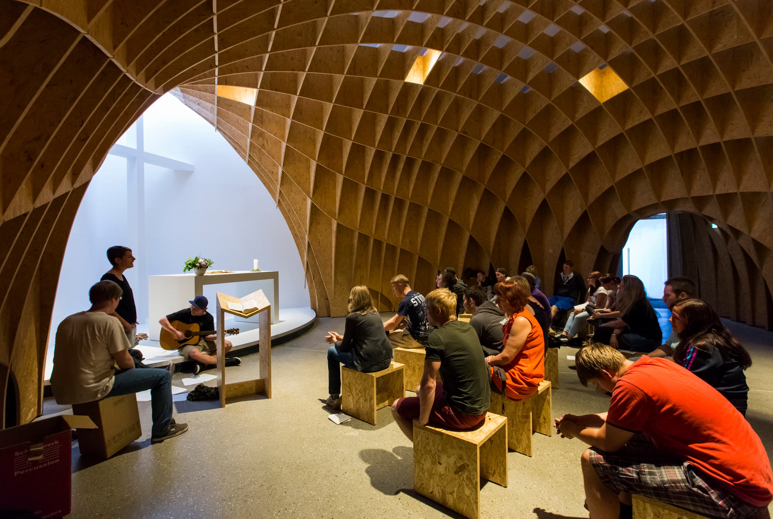 Innenansicht der Autobahnkirche Siegerland mit Holzstruktur und Gottesdienstbesuchern.