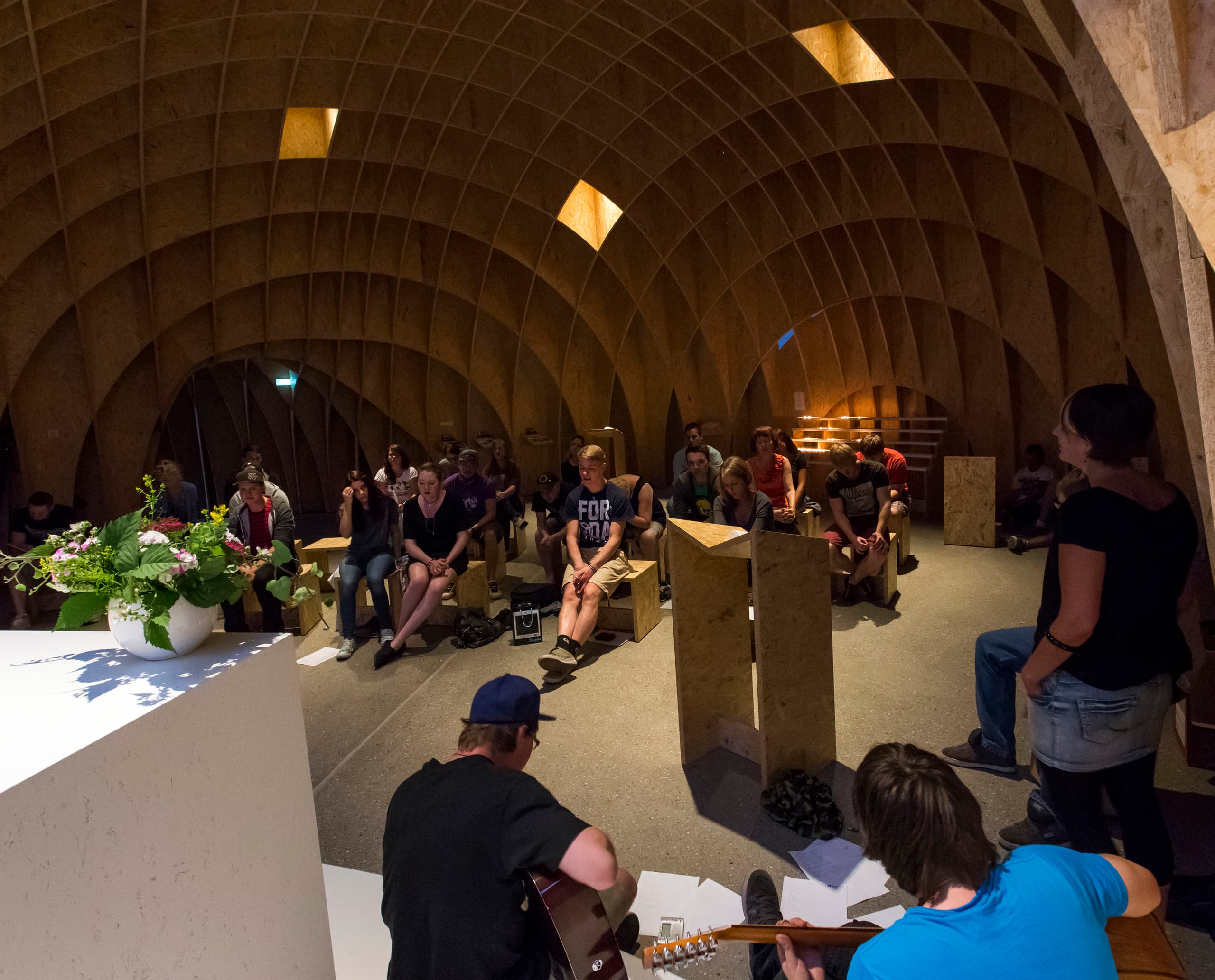 Innenraum der Siegerland Autobahnkirche mit Besuchern und Musikern, beleuchtet mit ERCO Licht.