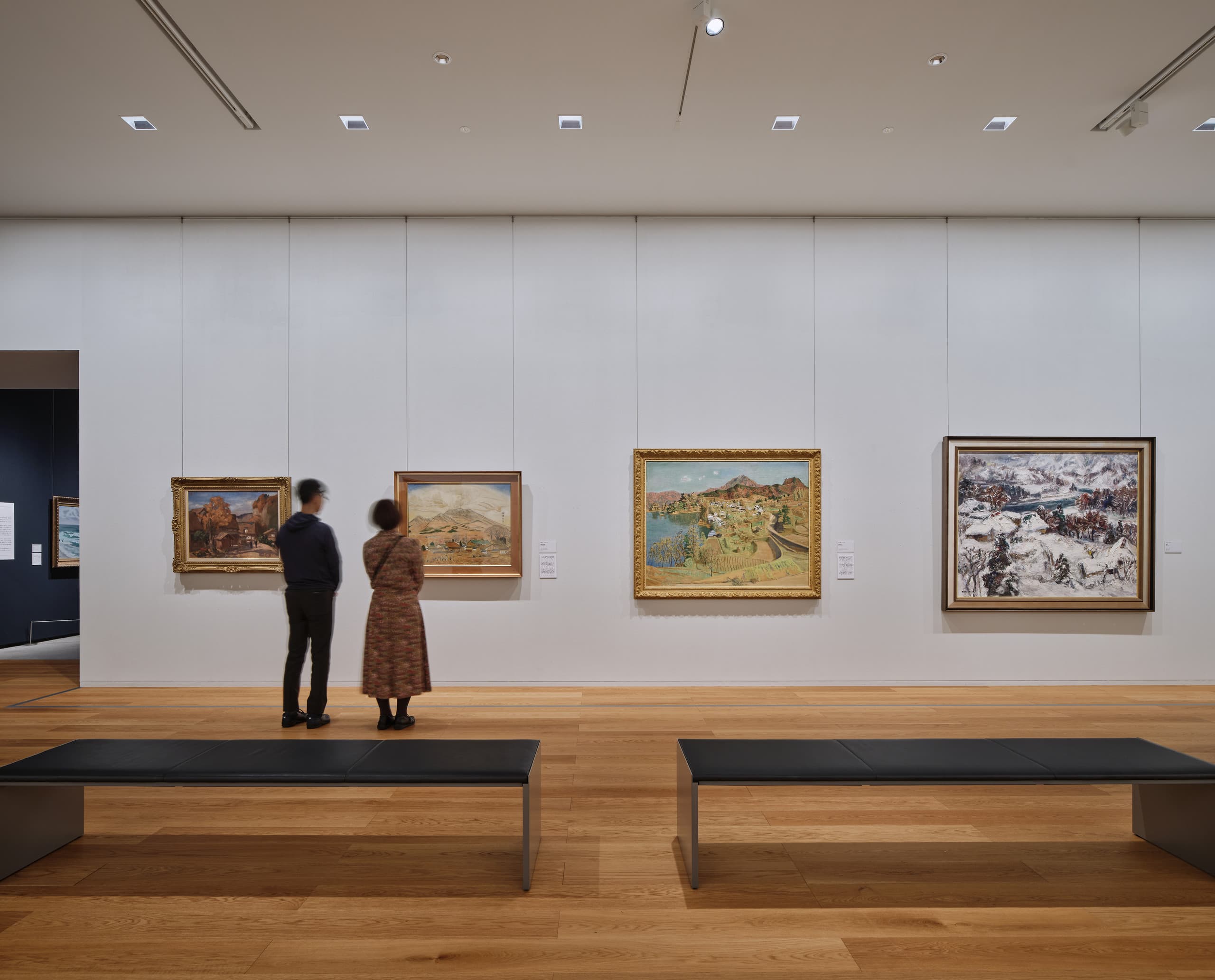 Zwei Menschen stehen in einem Museum vor einer Wand mit Gemälden.