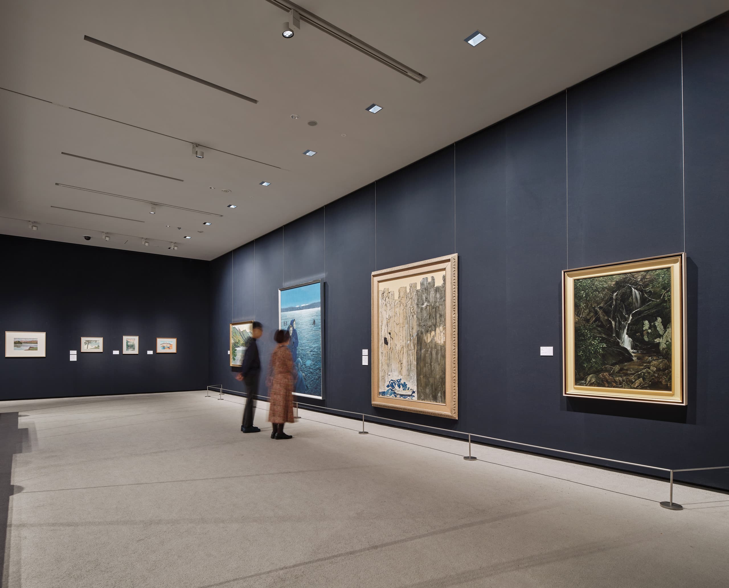Zwei Menschen stehen in einem Museum vor einer dunklen Wand mit Gemälden.