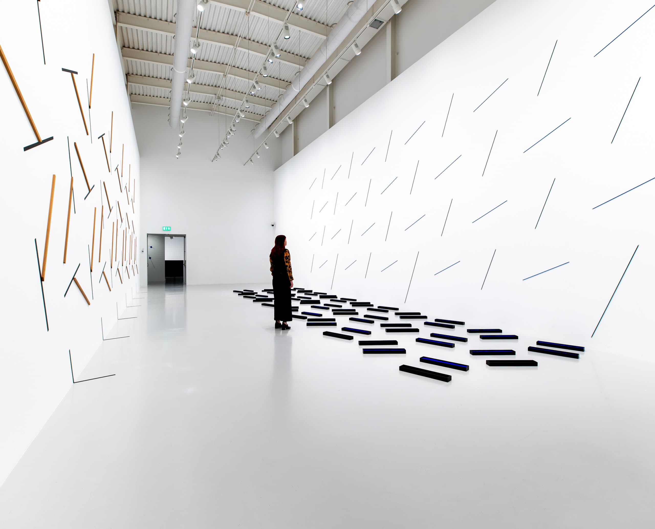 Weißer Ausstellungsraum mit blauen und schwarzen Brettern und einer Betrachterin.