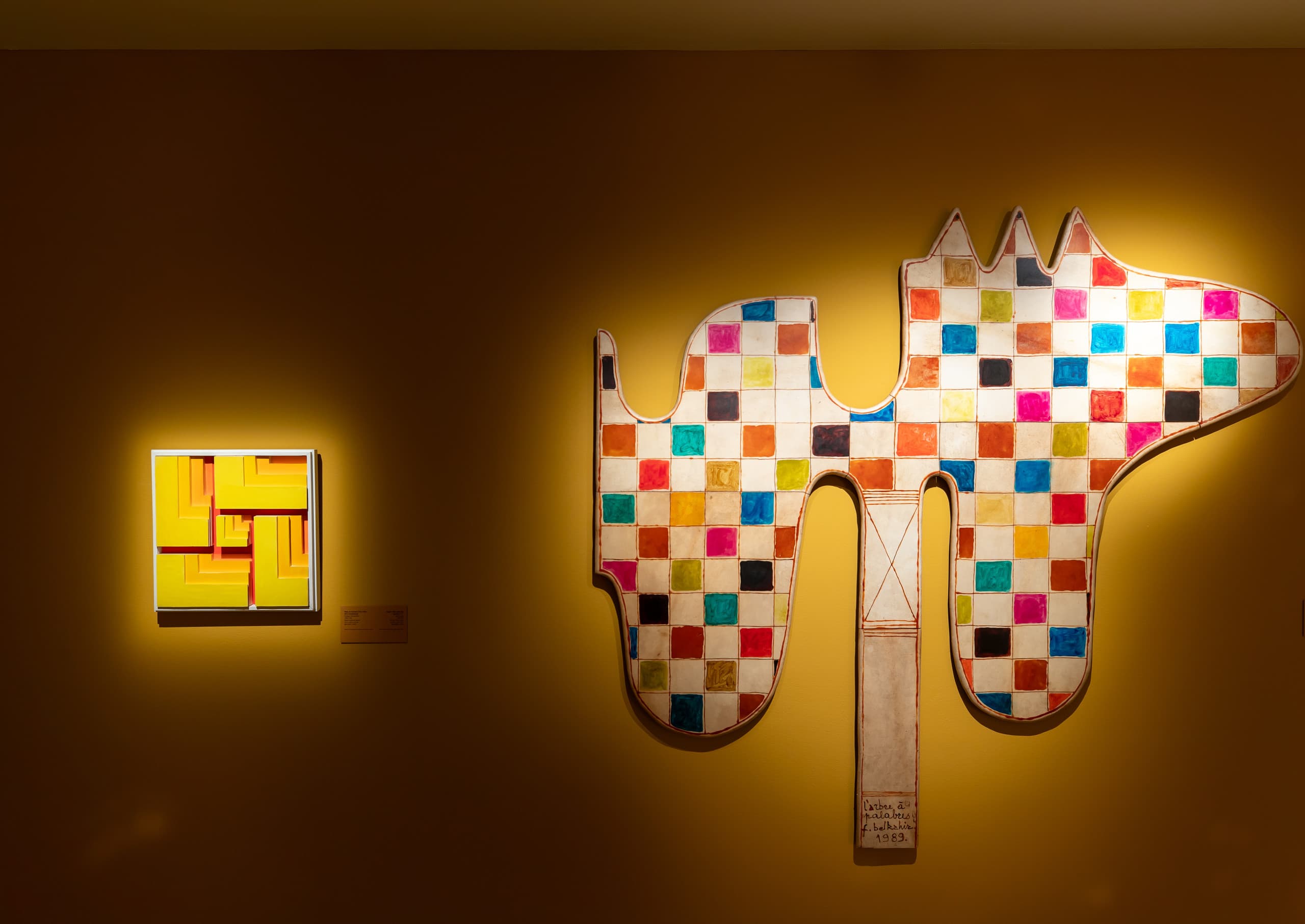 Mit Licht akzentuierte Kunstwerke auf gelber Wand.