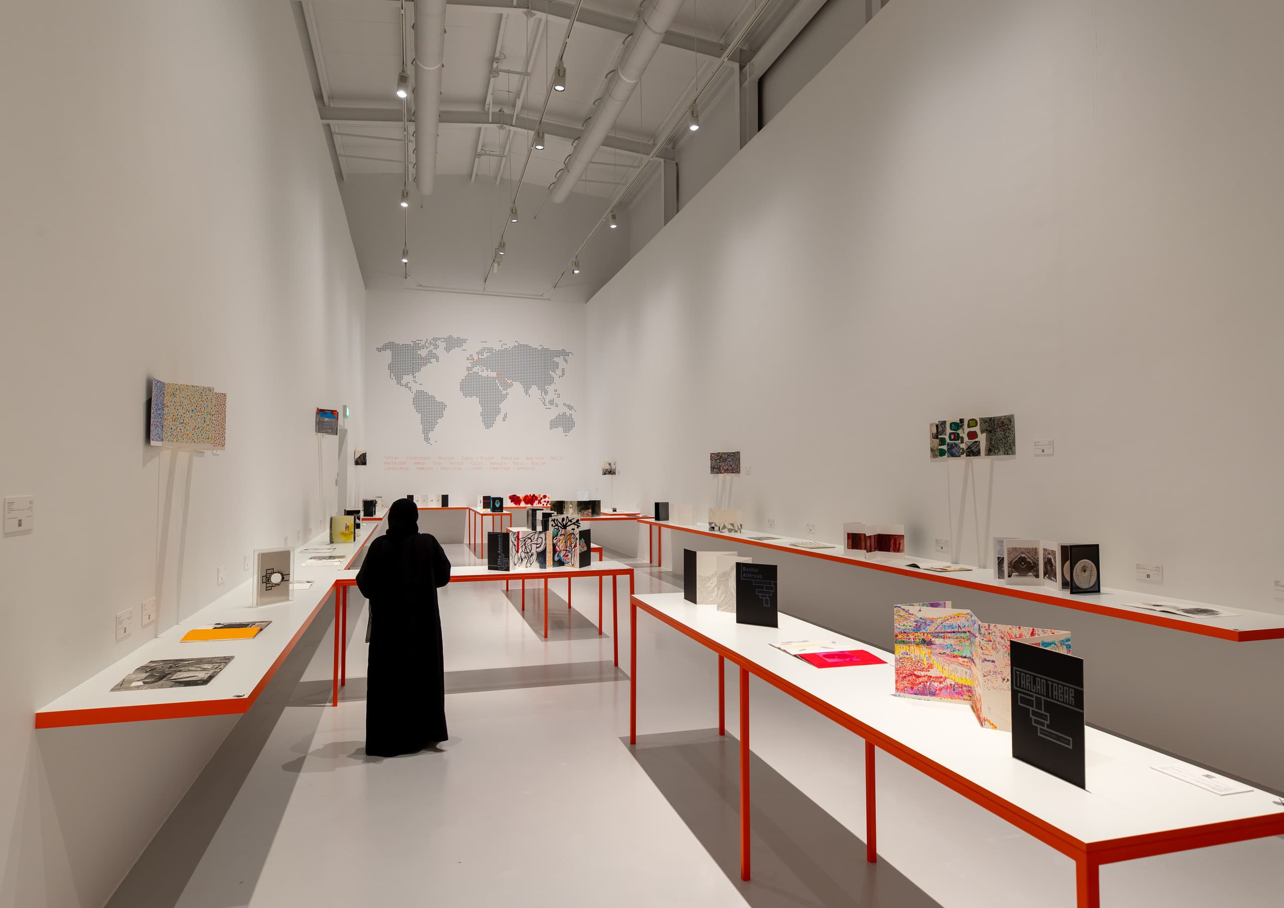Ausstellungsraum mit rot-weißen Tischen und Ausstellungsstücken.