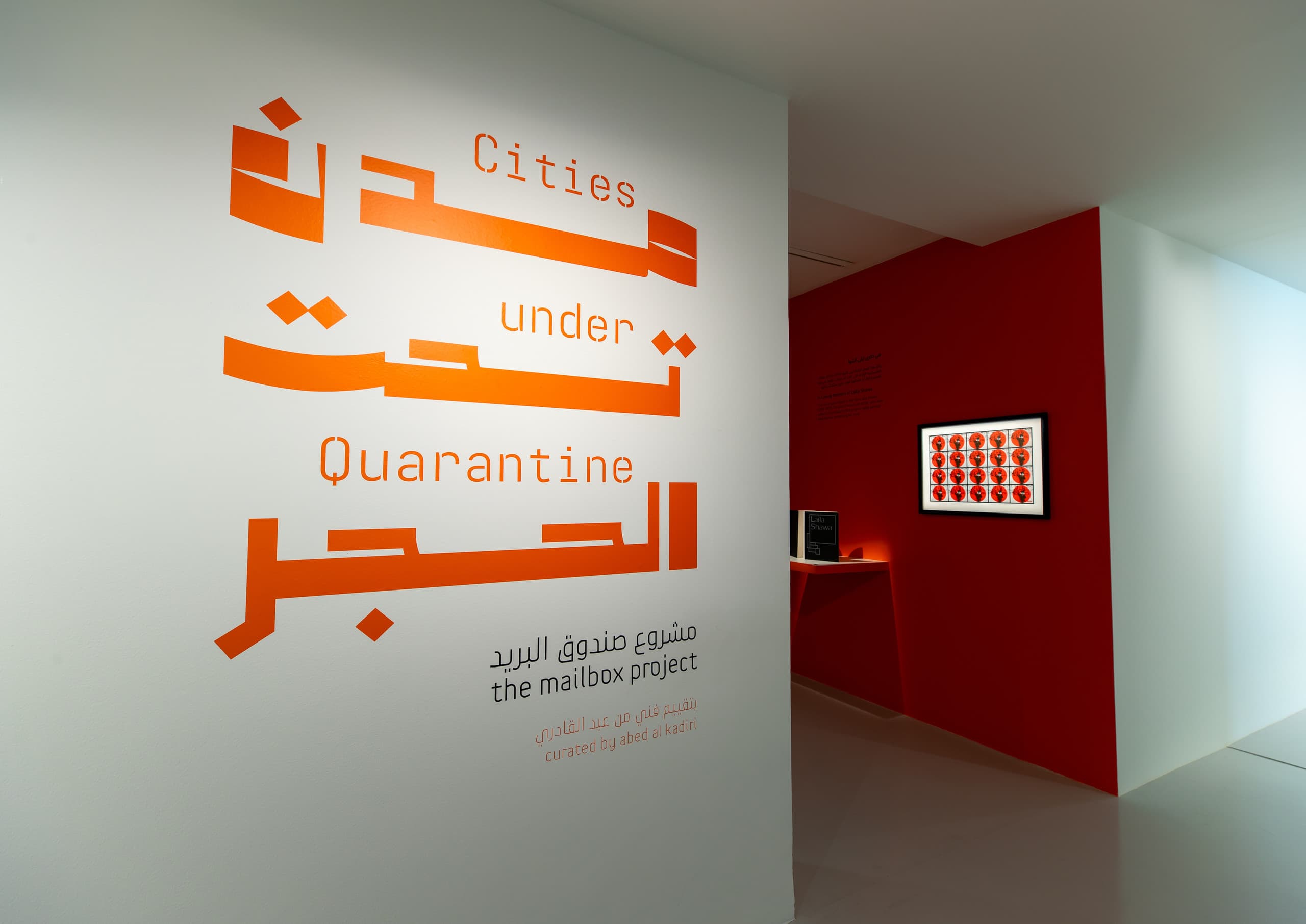 Ausstellungsraum mit roter Wand und orangener Aufschrift auf weißer Wand.
