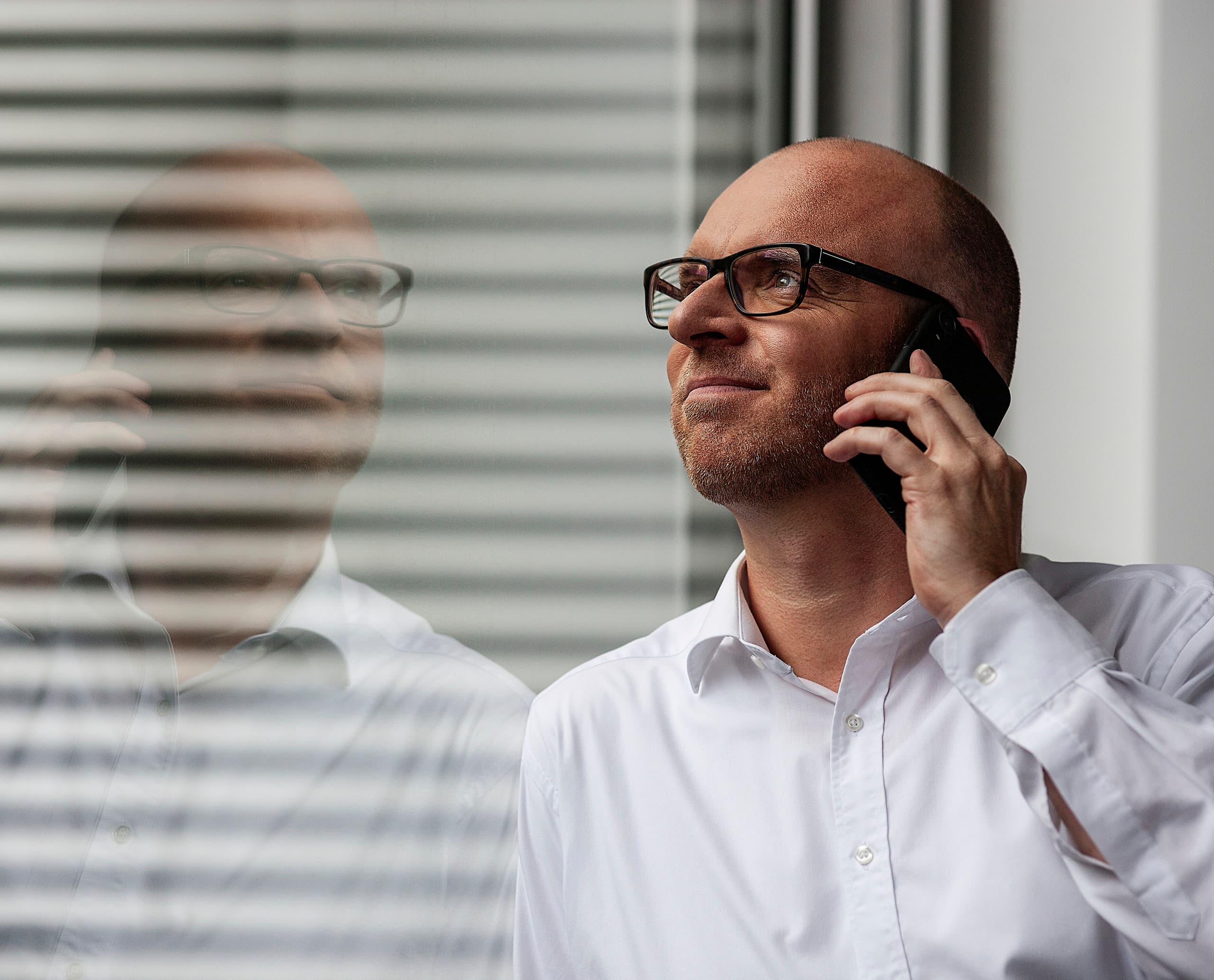Mann telefoniert, Spiegelung im Fenster. ERCO Partner für erfolgreiche Zusammenarbeit.