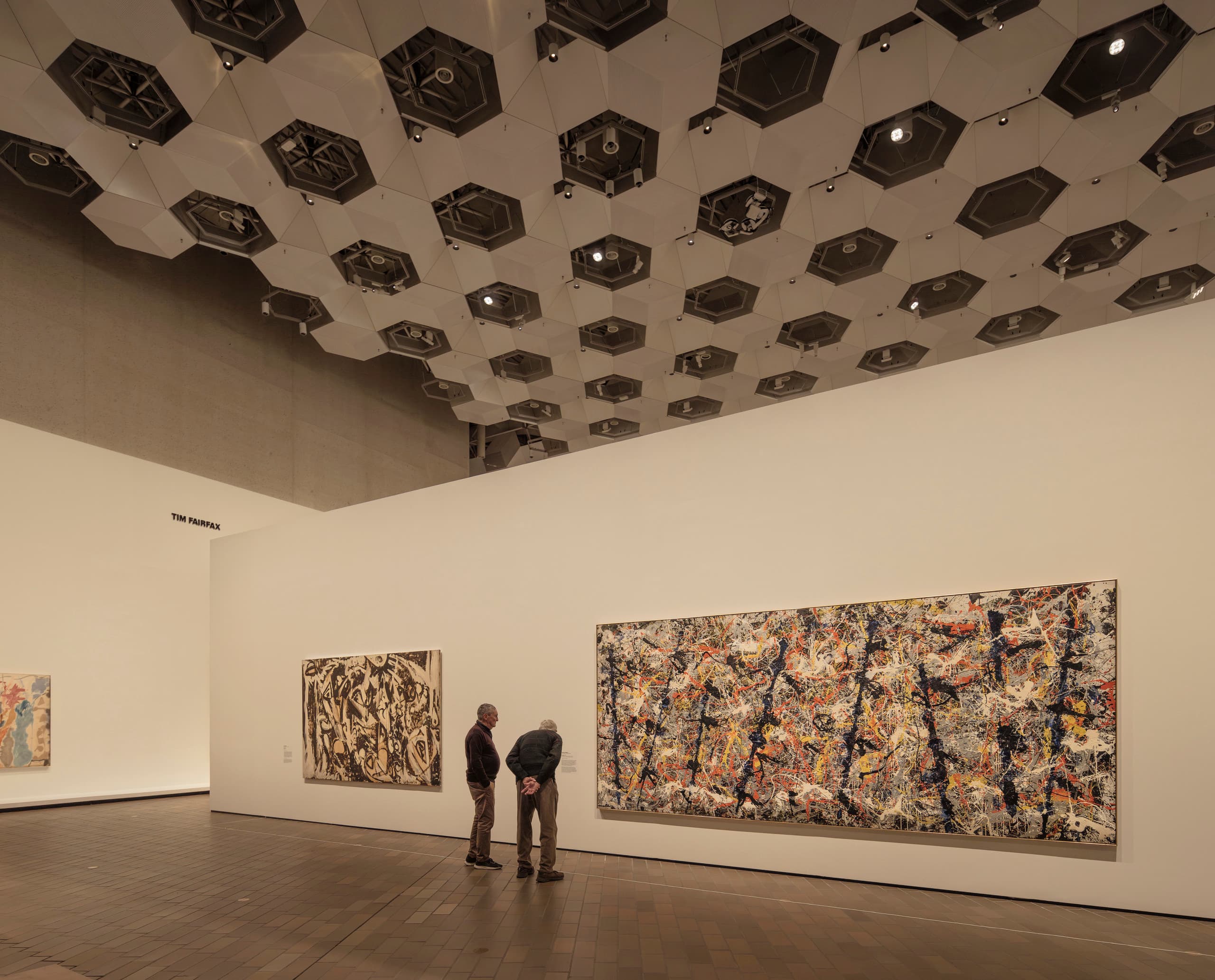 Ausstellungsraum mit großem Gemälde an der Wand, davor stehen zwei Menschen.