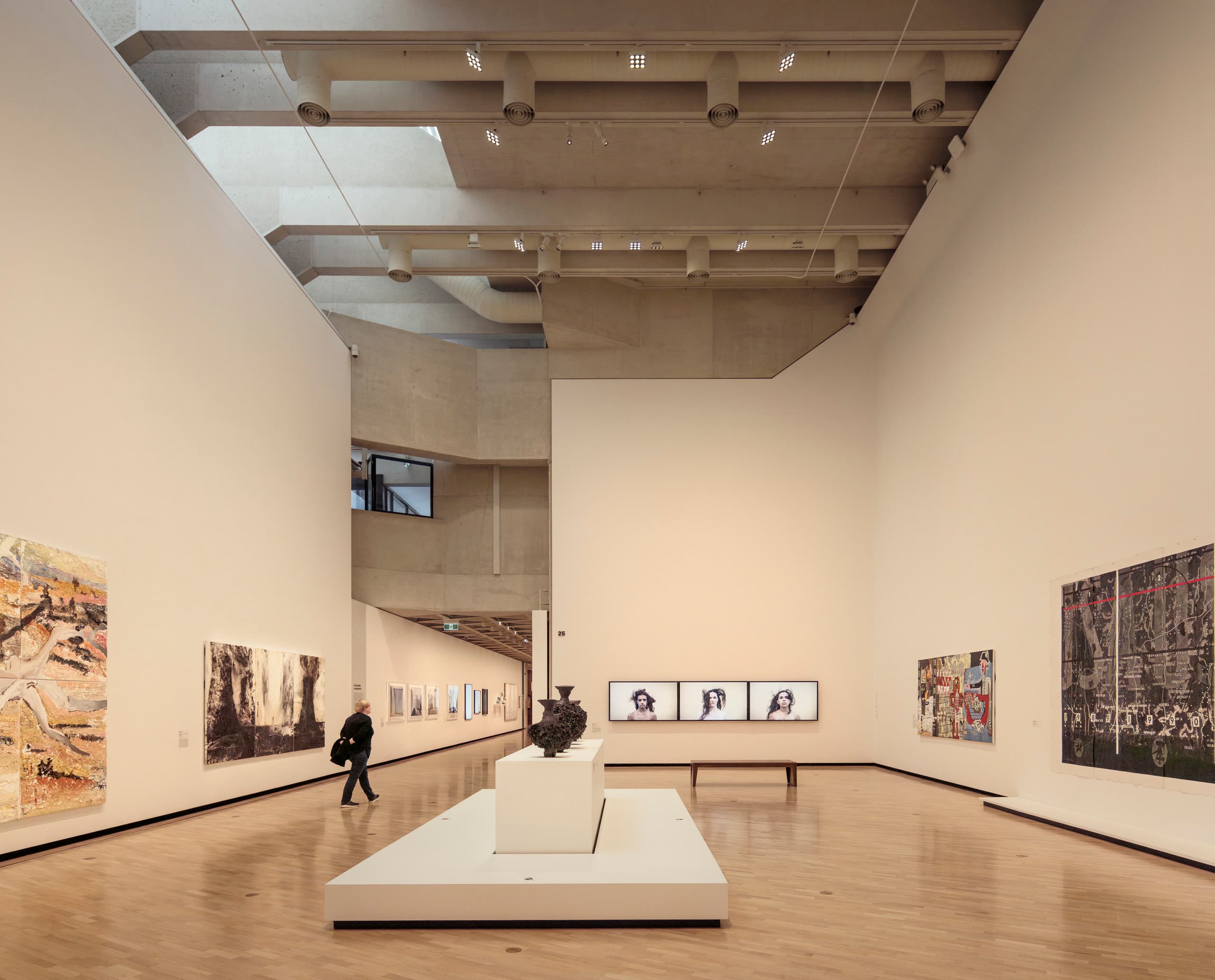 Ausstellungsraum mit hoher Decke, Gemälden und Skulptur in der Mitte.
