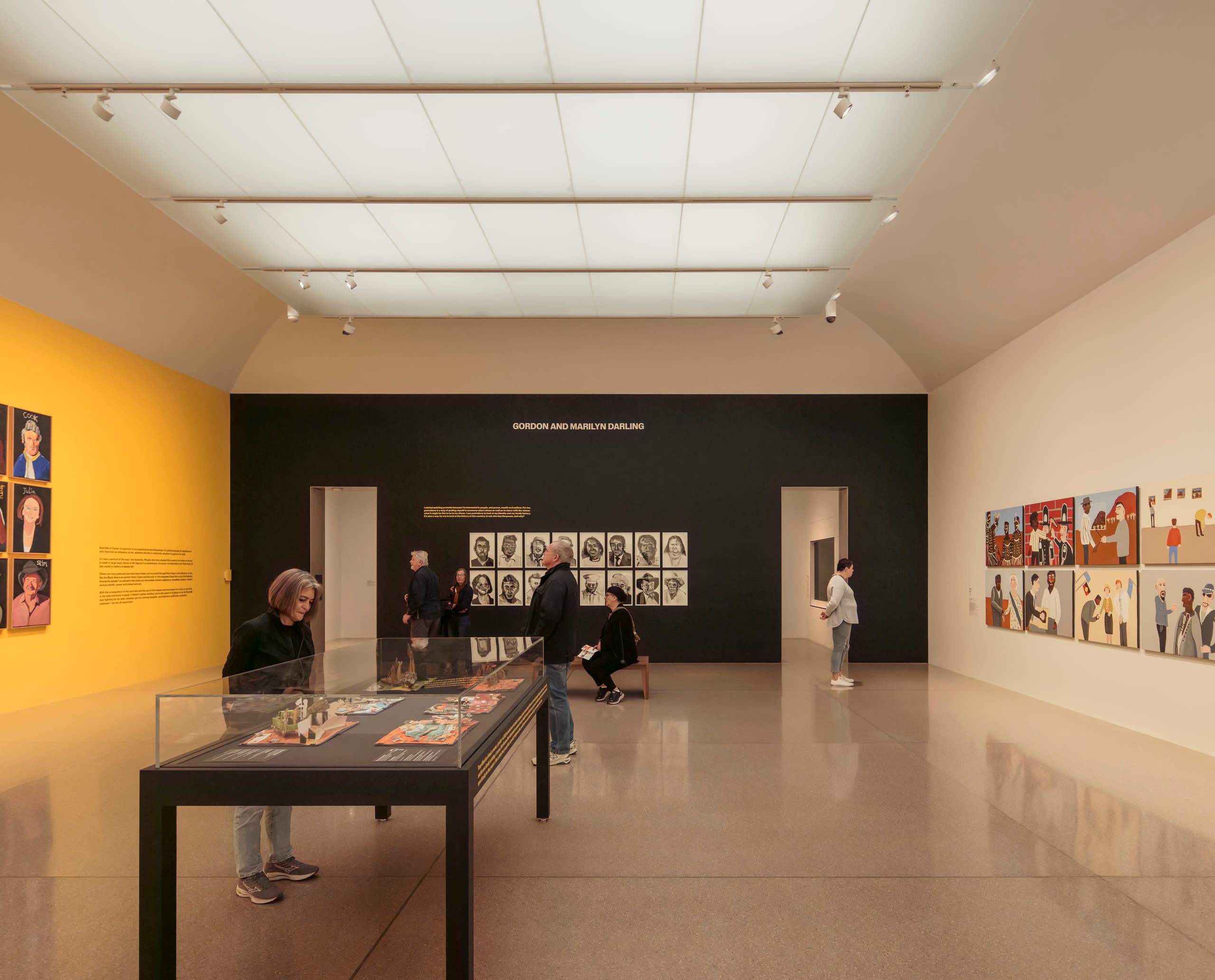 Ausstellungsraum mit schwarzer und Gelber Wand, Menschen bewegen sich durch den Raum.