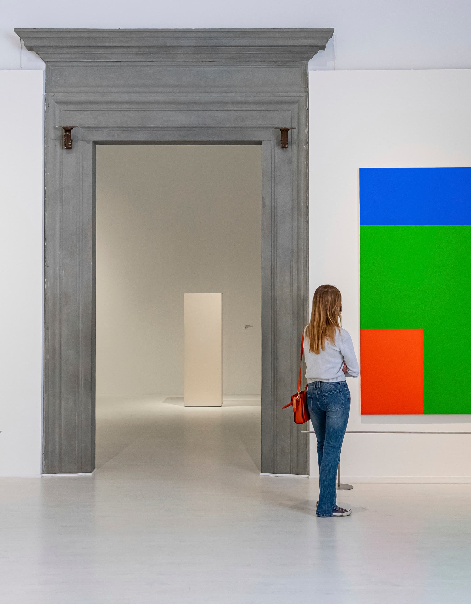 Frau betrachtet Gemälde mit Farbkontrasten in einer Kunstgalerie. Lichtdesign.