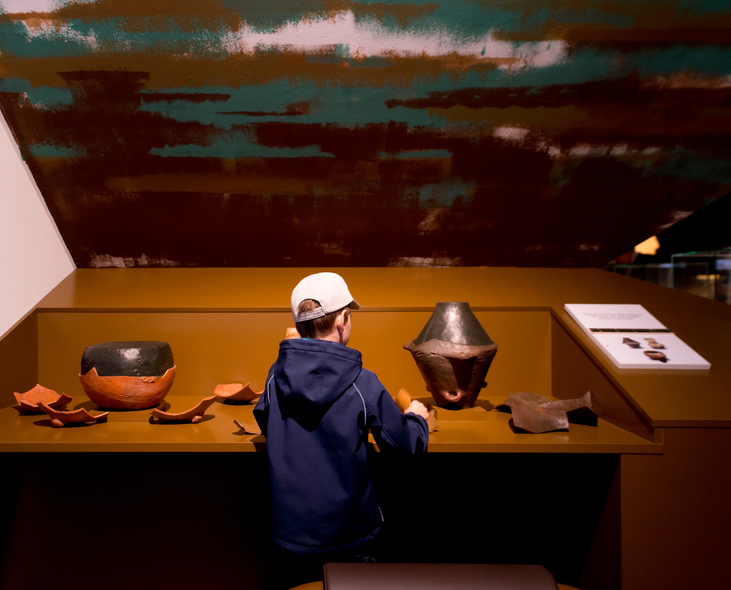 Junge interagiert mit archäologischen Fundstücken im MAMUZ Museum, Mistelbach.