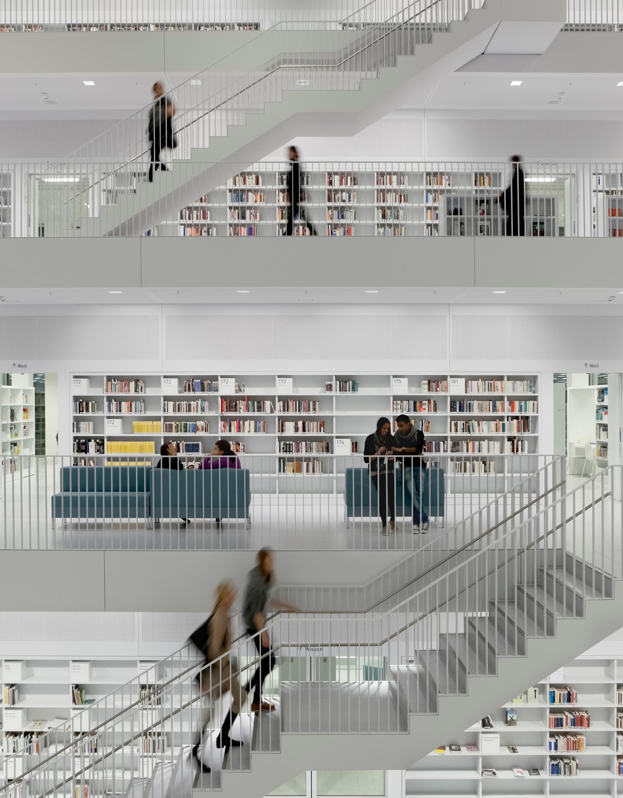 Innenansicht einer Bibliothek mit mehreren Etagen, Treppen und Regalen voller Bücher, beleuchtet mit ERCO Licht.
