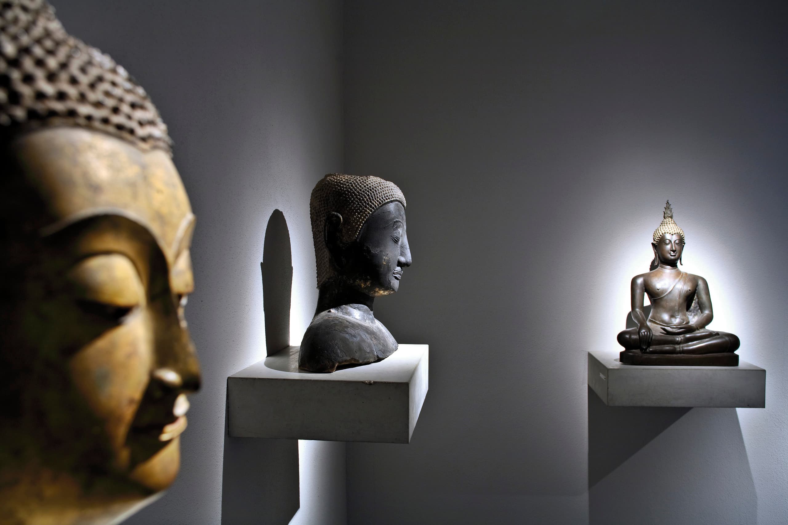 Buddha-Statuen, hervorgehoben durch gerichtetes Licht in einer Museumsausstellung.