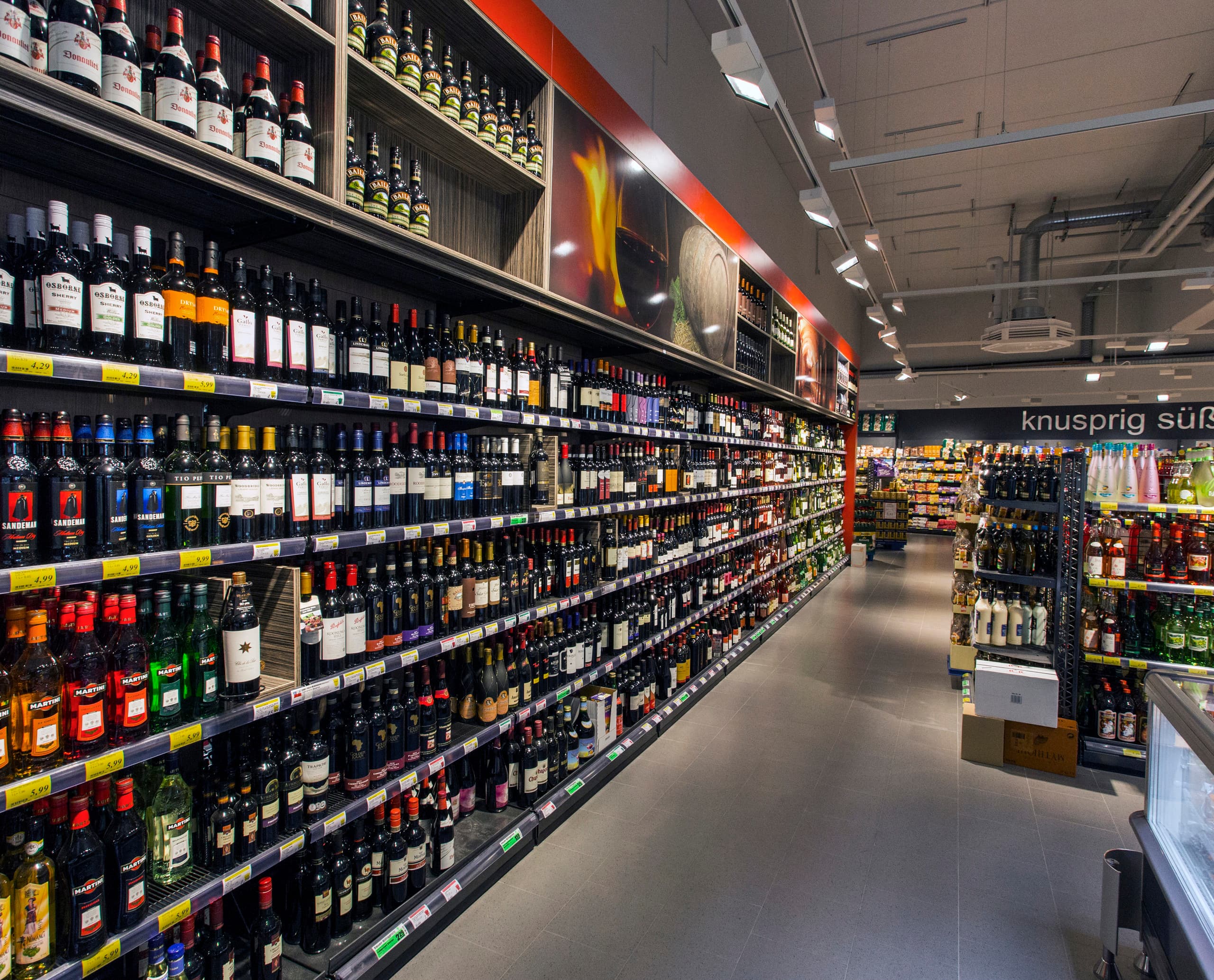 Regale mit Wein und Spirituosen im REWE-Supermarkt, beleuchtet mit ERCO Opton LED Strahlern für Akzentbeleuchtung.