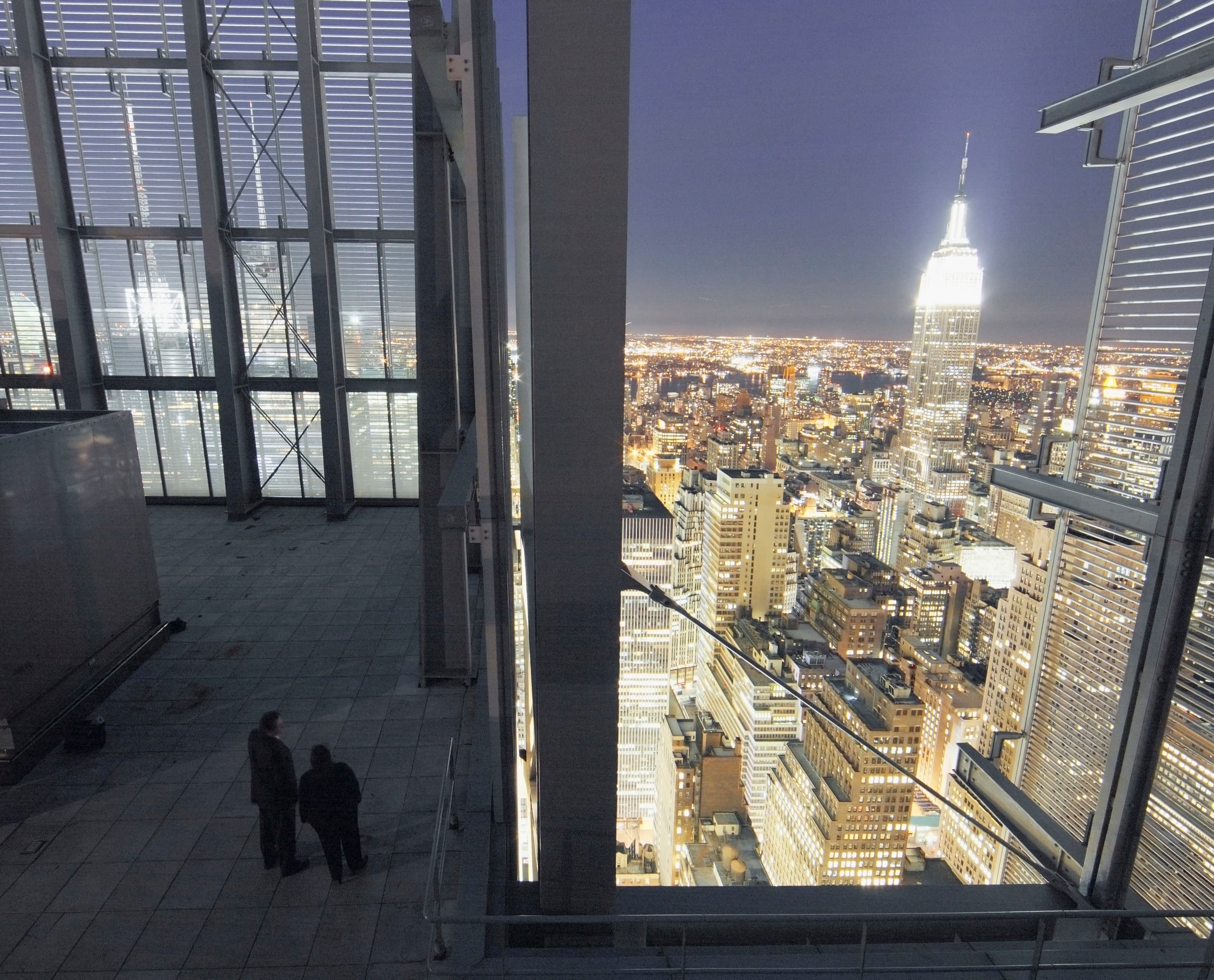 Blick auf das Empire State Building bei Nacht, gesehen durch eine moderne Fensterstruktur.