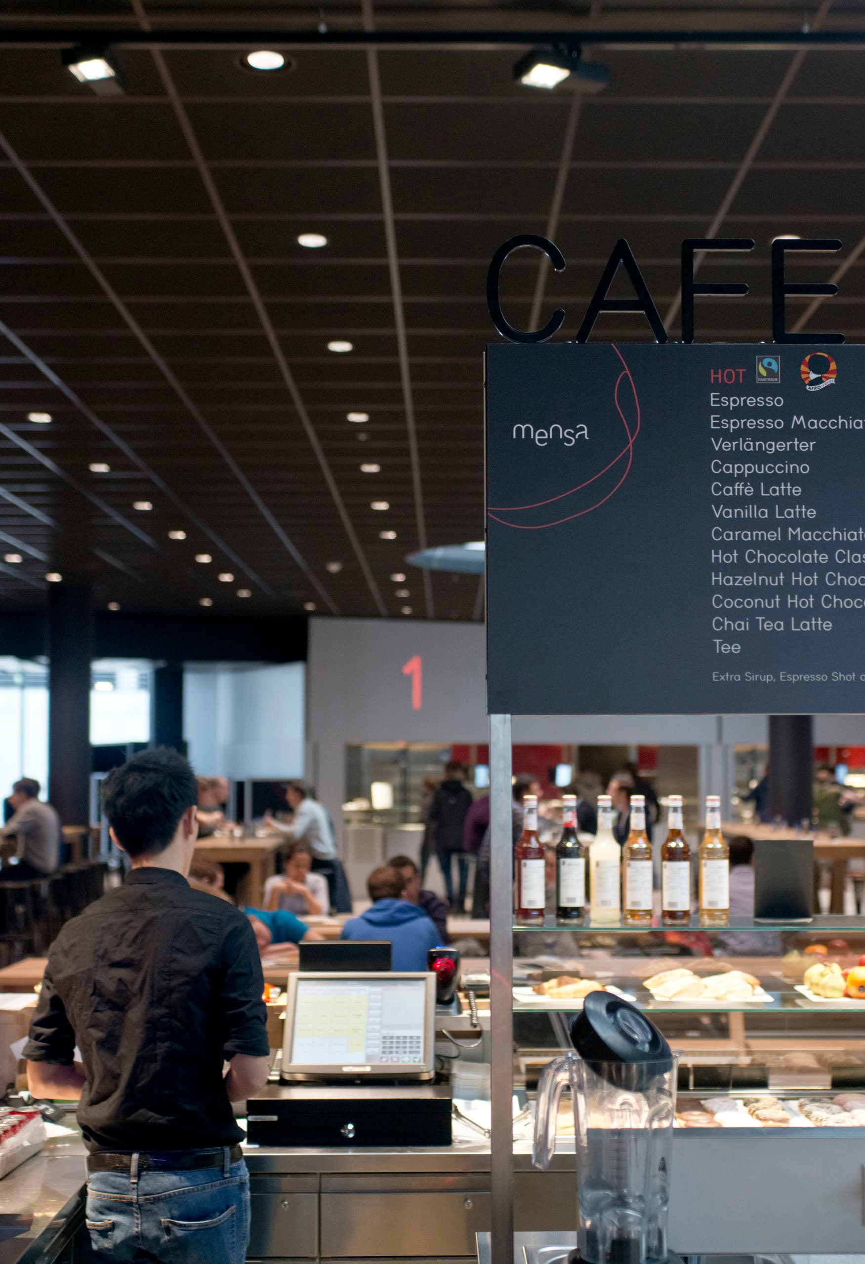 Cafeteria der Wirtschaftsuniversität Wien mit Speisekarte und warmen Speisen unter ERCO LED-Beleuchtung.