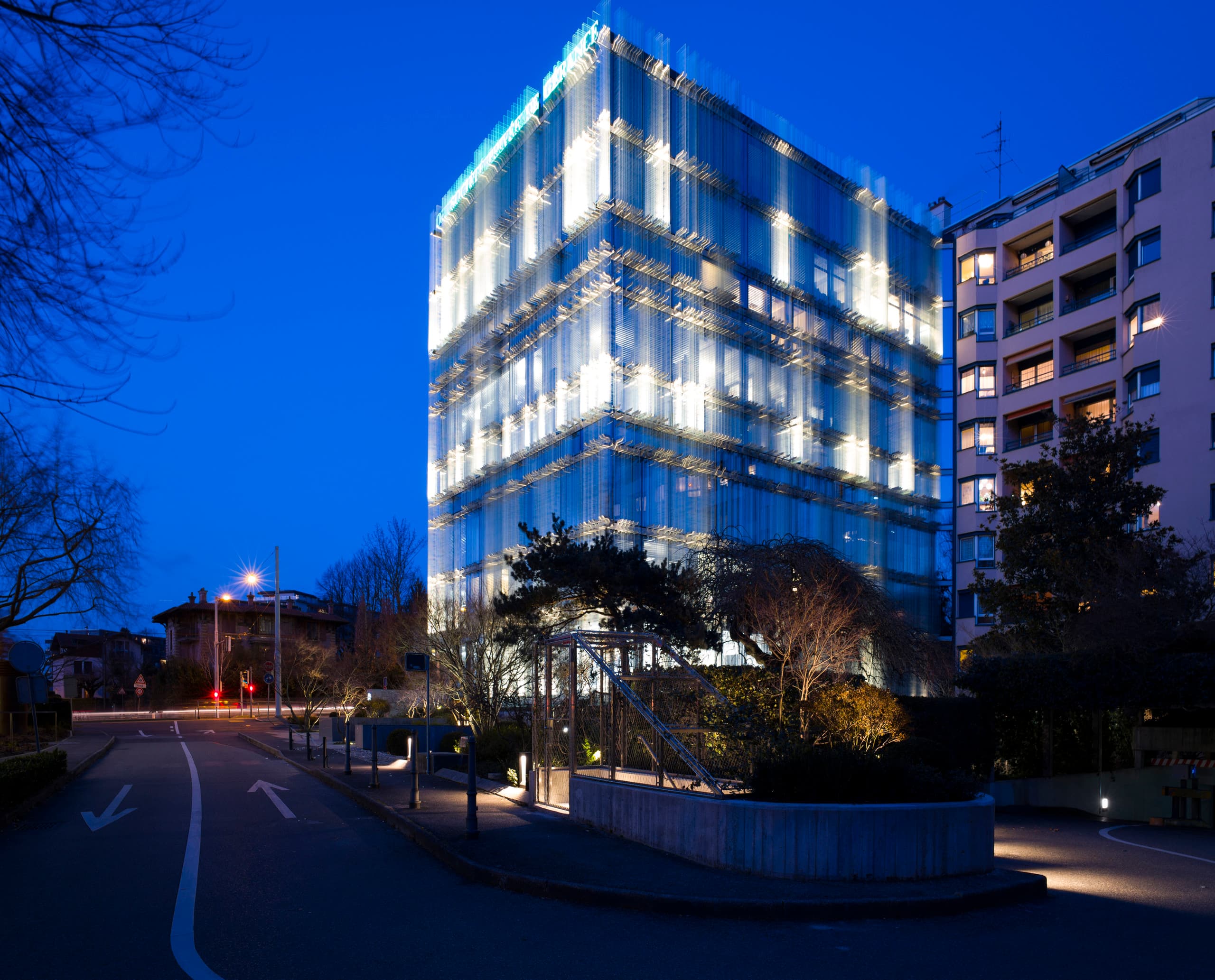 SPG Hauptsitz Genf mit ERCO LED Fassadenbeleuchtung und Glaslamellen bei Nacht.