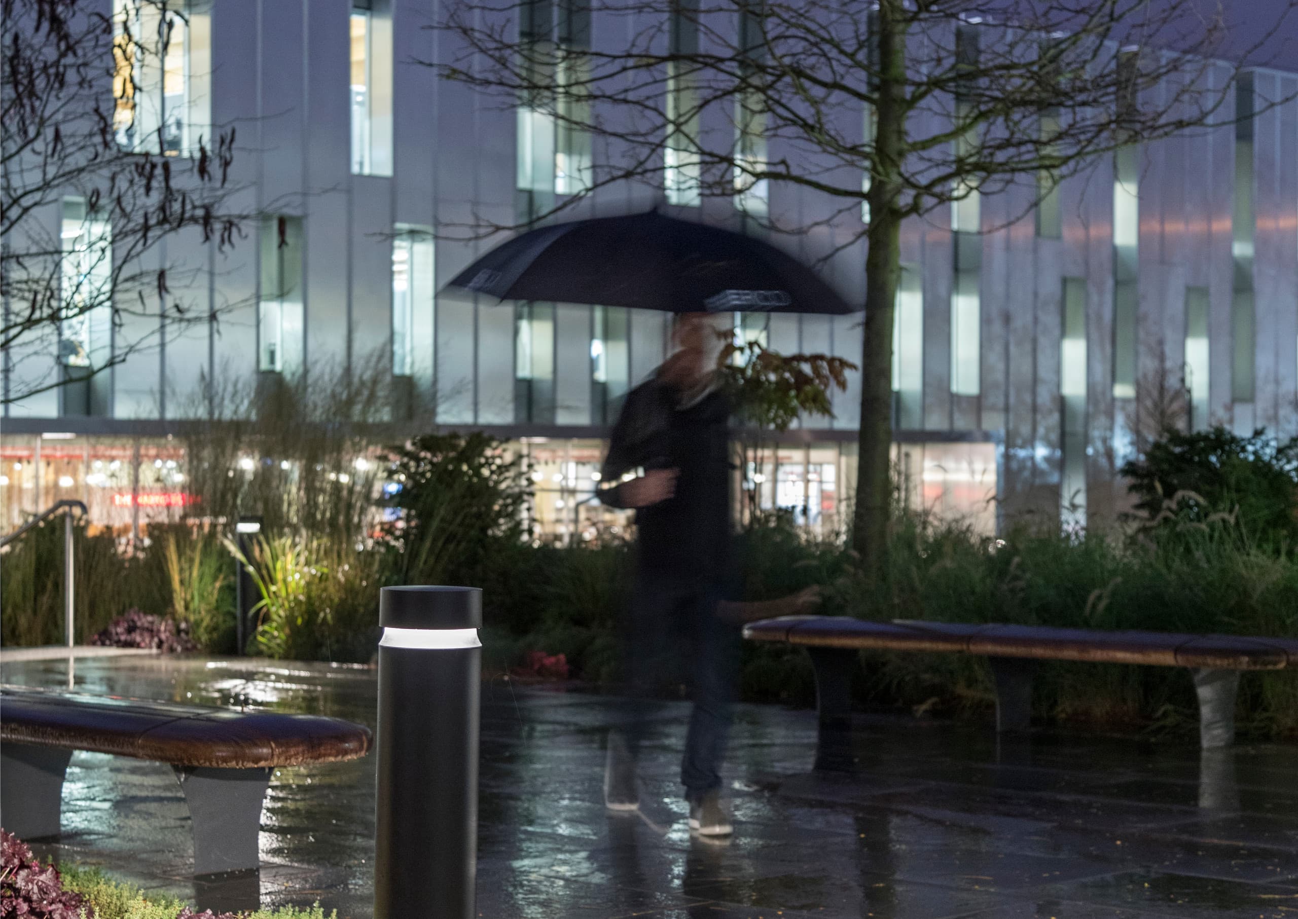 ERCO Pollerleuchte beleuchtet einen regnerischen Parkweg und sorgt für Orientierung und Sicherheit im Dunkeln.