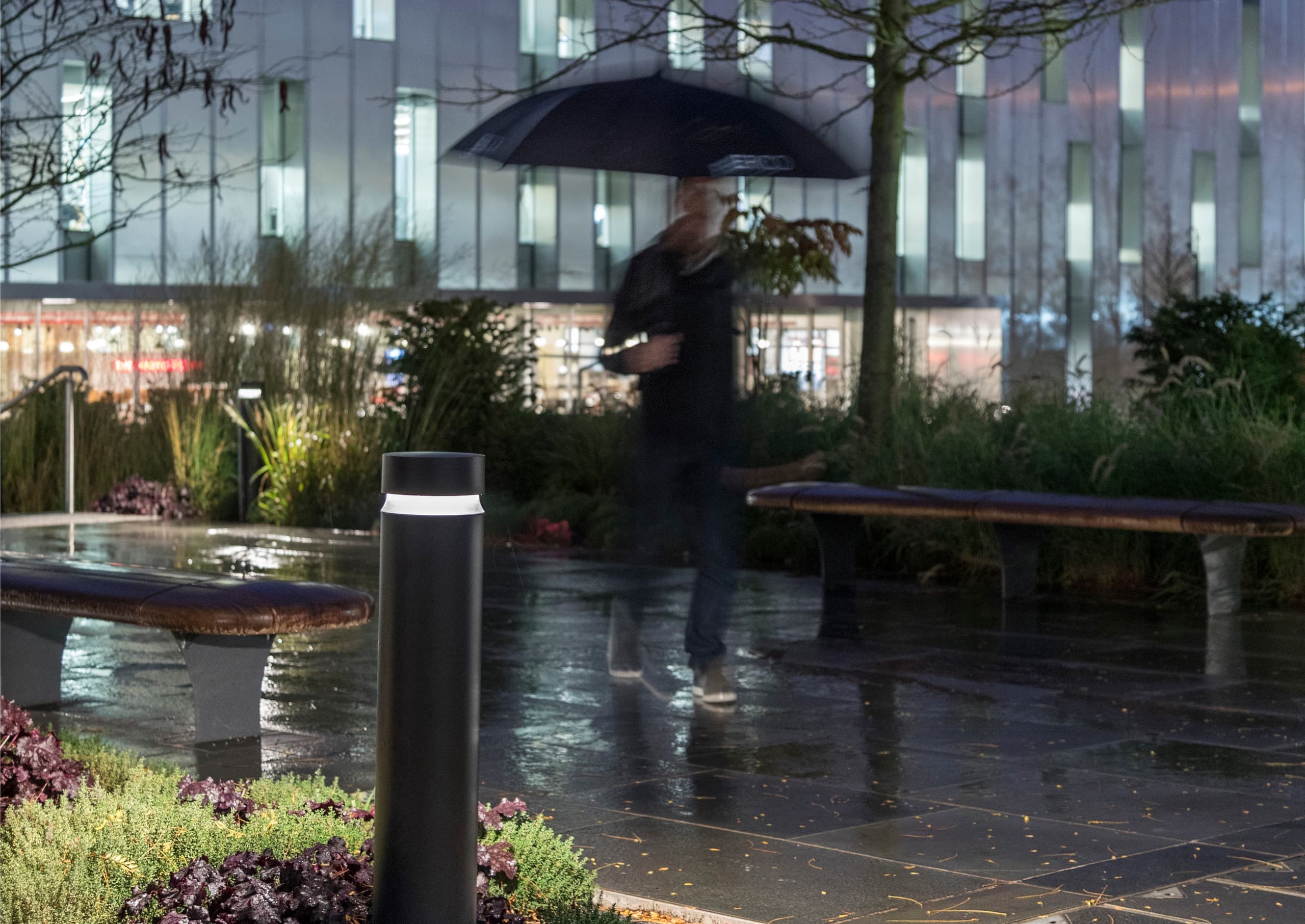 ERCO Pollerleuchte beleuchtet einen regnerischen Parkweg und sorgt für Orientierung und Sicherheit im Dunkeln.
