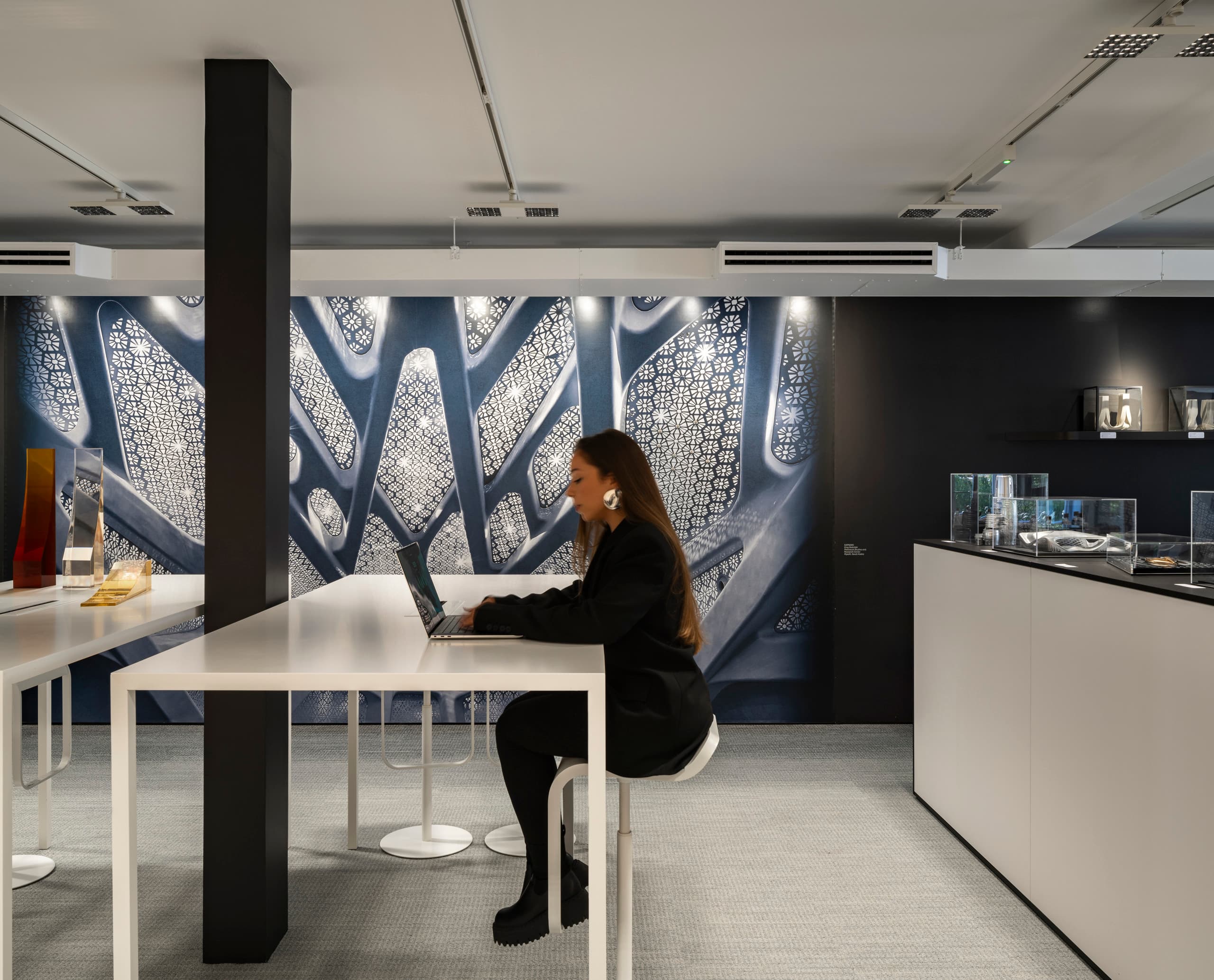 ERCO Beleuchtung im Zaha Hadid Büro: Mitarbeiterin arbeitet am Laptop in modernem, gut beleuchteten Büro.