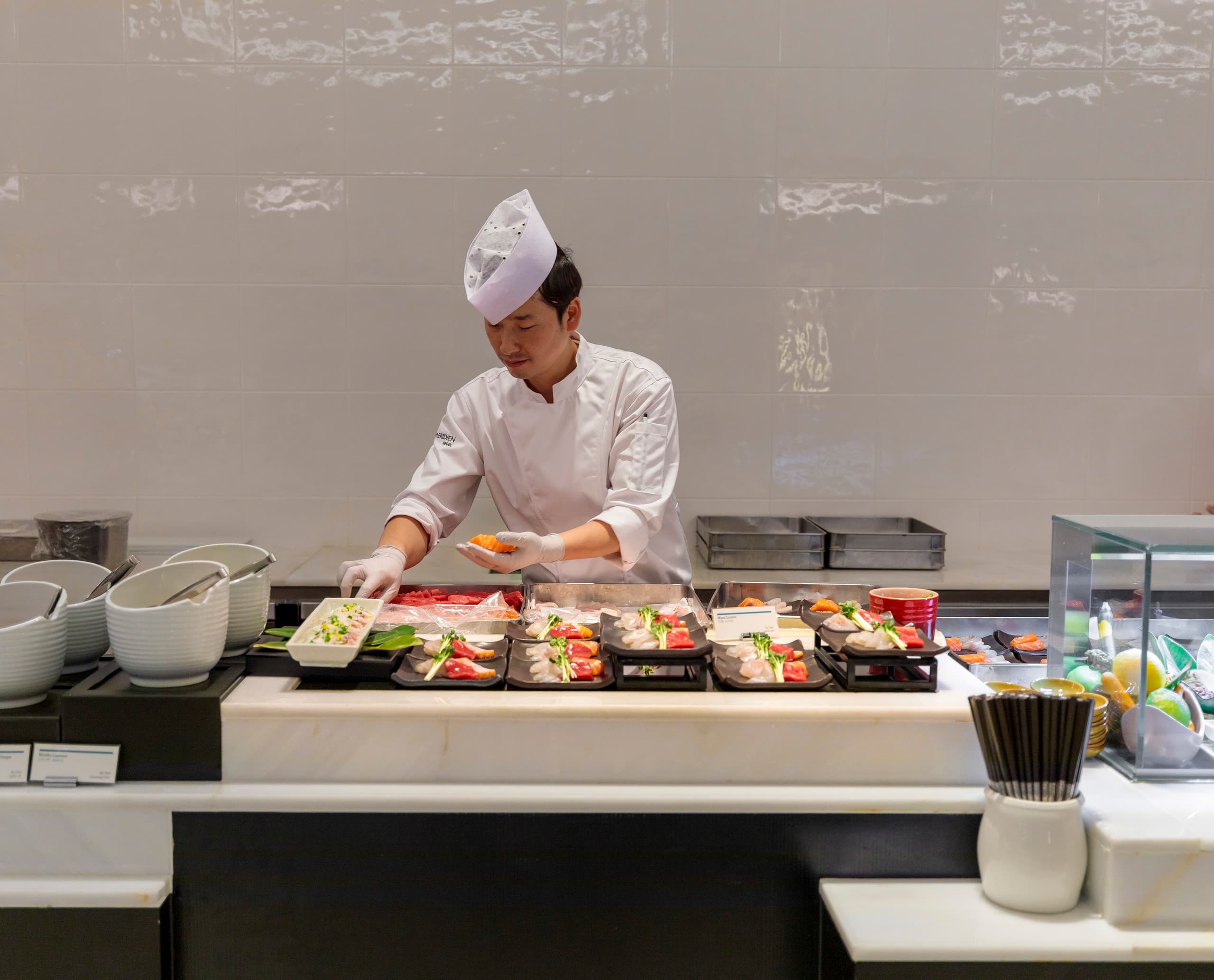 Sushi-Koch im Le Méridien Seoul bereitet Speisen zu, akzentuiert durch ERCO-Beleuchtung für einladende Gastfreundschaft.
