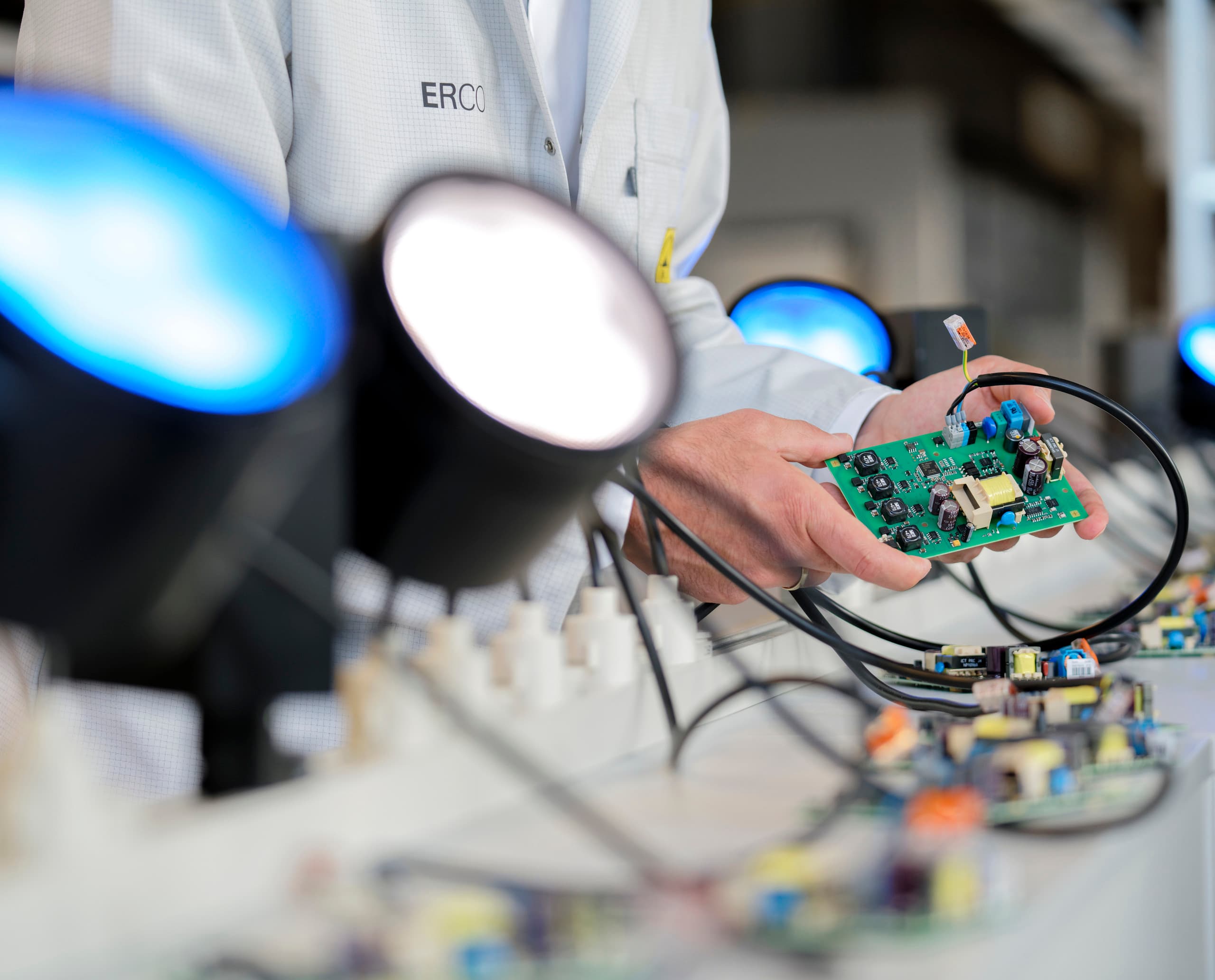 ERCO Mitarbeiter prüft eine Platine unter LED-Leuchten, Qualitätssicherung.