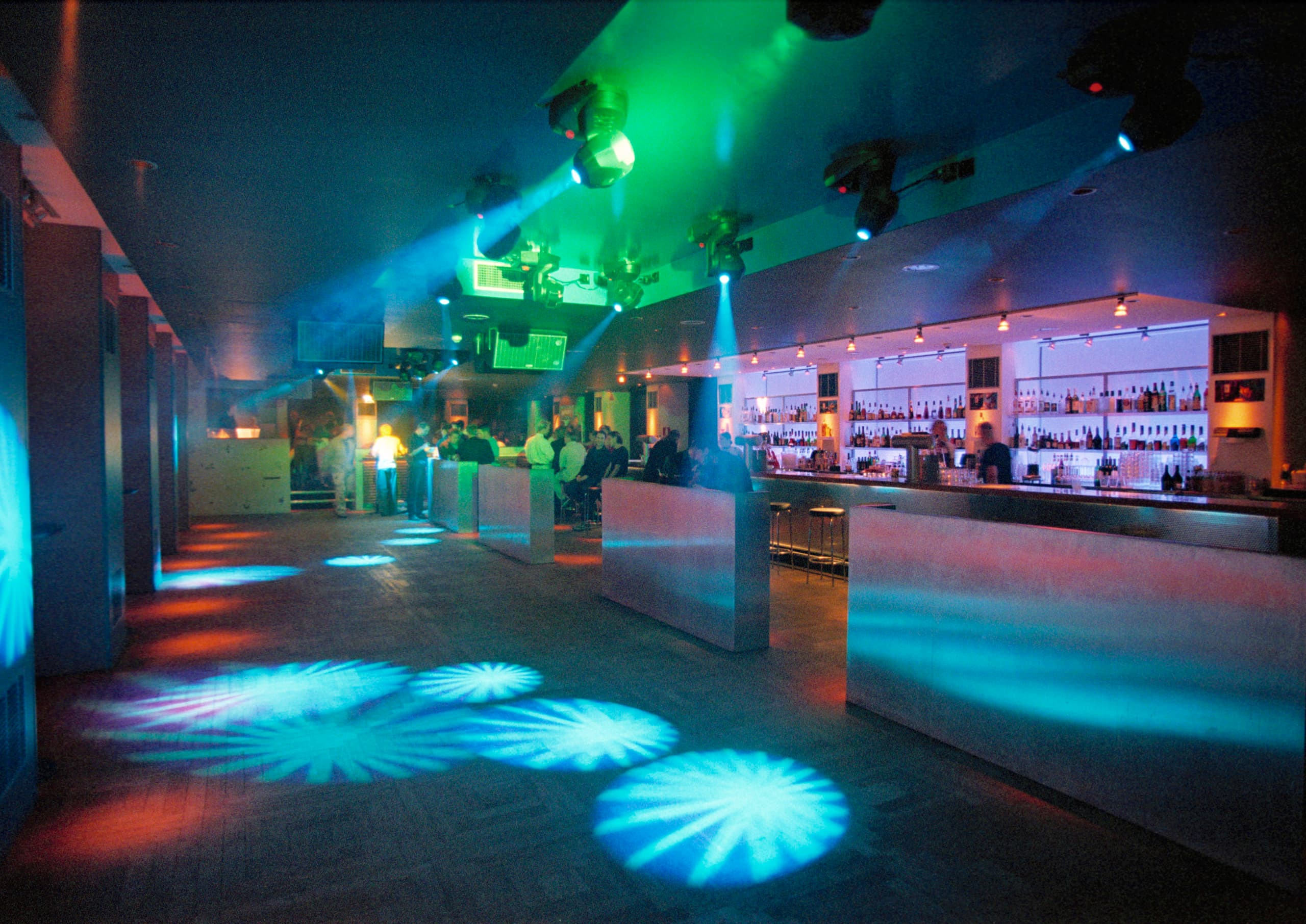 Farbige ERCO Lichtprojektionen in einer Bar, die eine stimmungsvolle Atmosphäre durch Lichtmischung erzeugt.