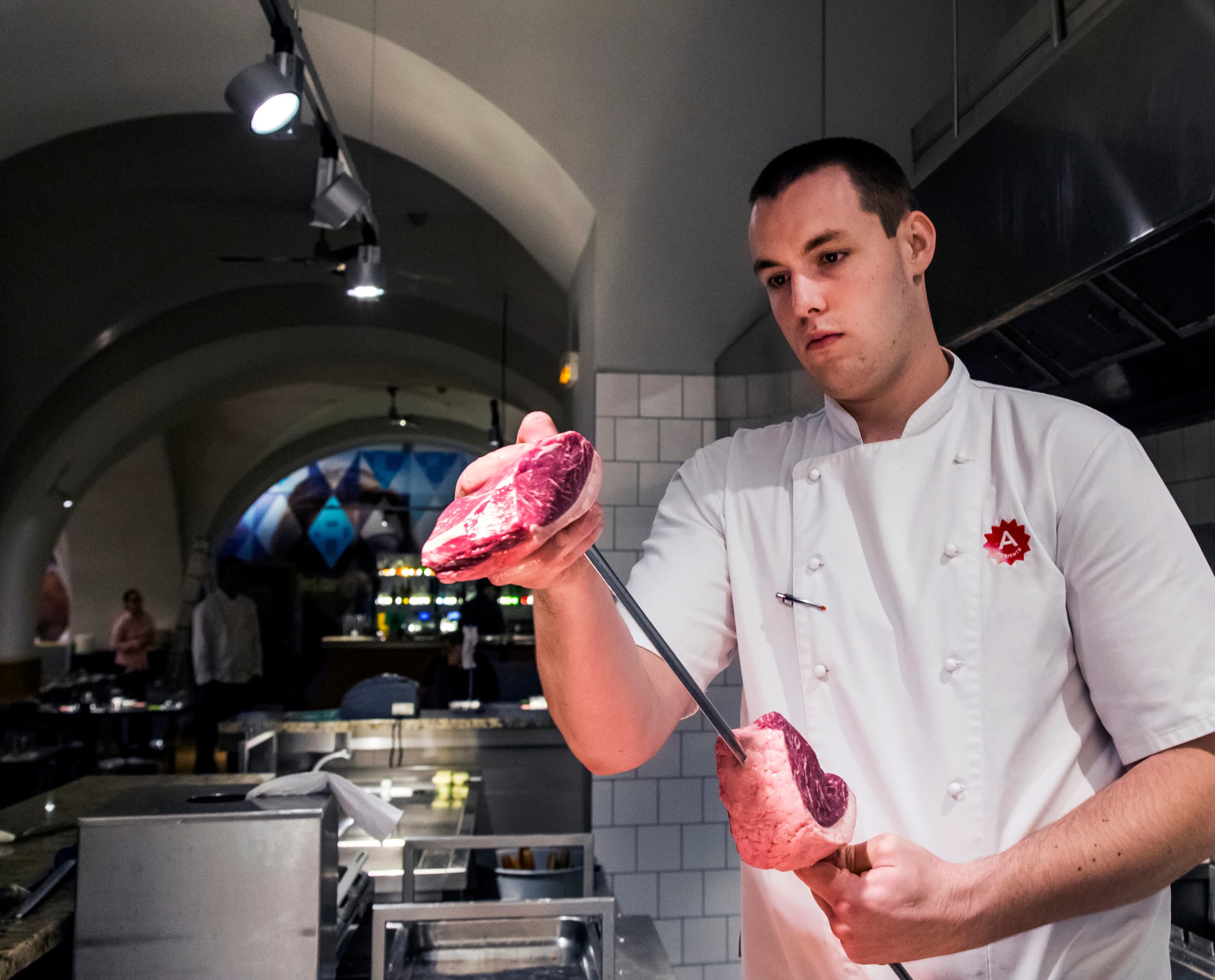 Koch im Ambiente Brasileiro Restaurant mit rohem Fleisch am Spieß, beleuchtet mit ERCO LED-Strahlern.