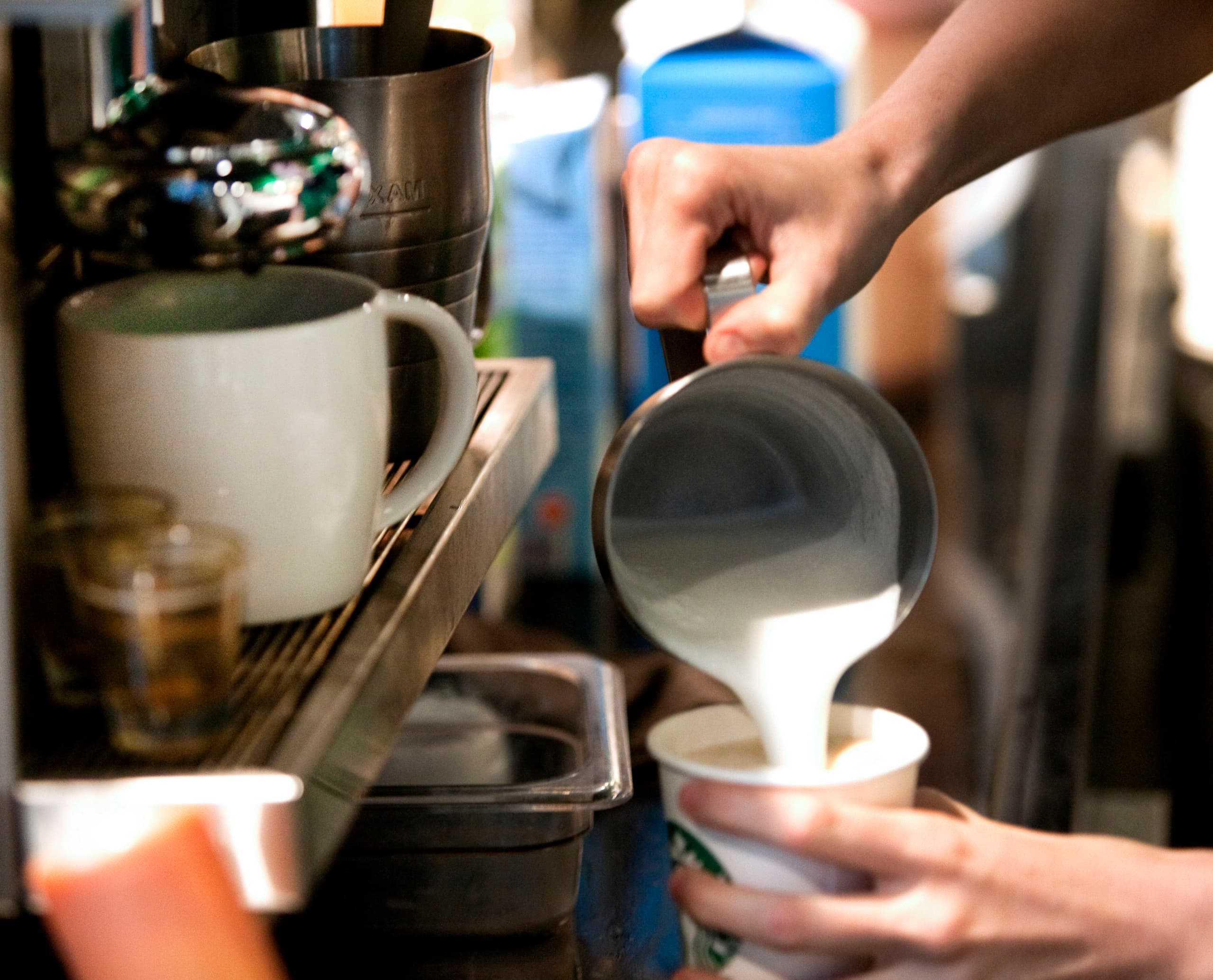 Einschenken von Milch in einen Starbucks Kaffee, Teil des anspruchsvollen Beleuchtungskonzepts.