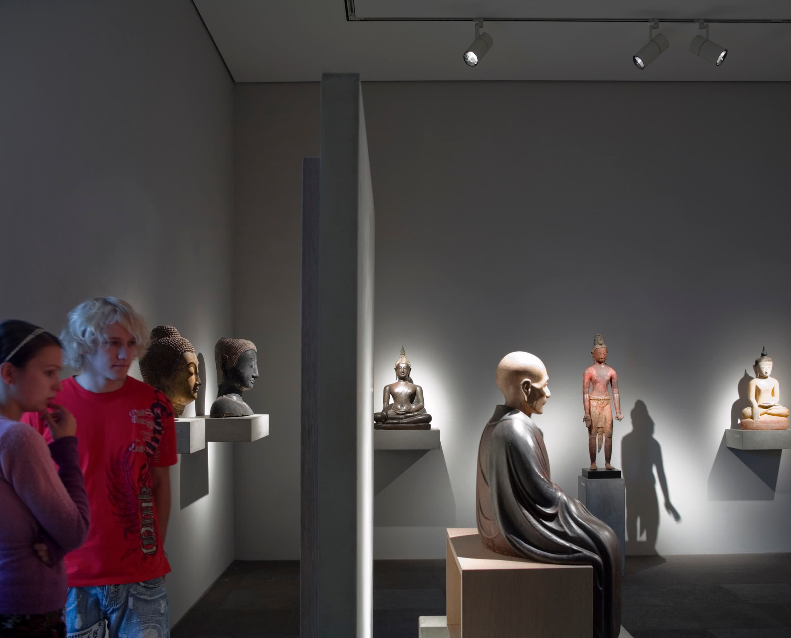 Besucher betrachten Buddha-Statuen im Louvre-Lens, beleuchtet mit ERCO LED-Lichtern.