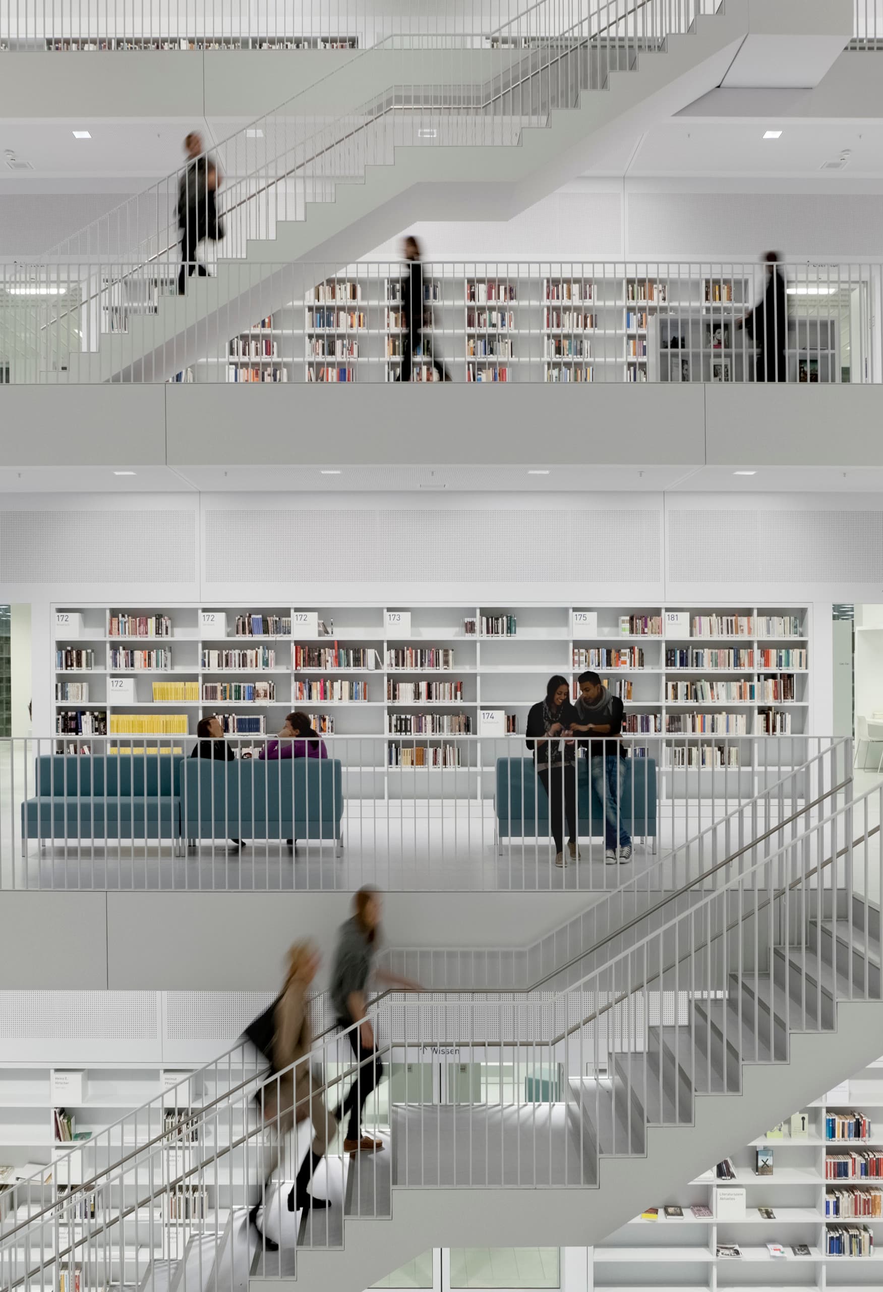 Innenansicht einer Bibliothek mit mehreren Etagen, Treppen und Regalen voller Bücher, beleuchtet mit ERCO Licht.