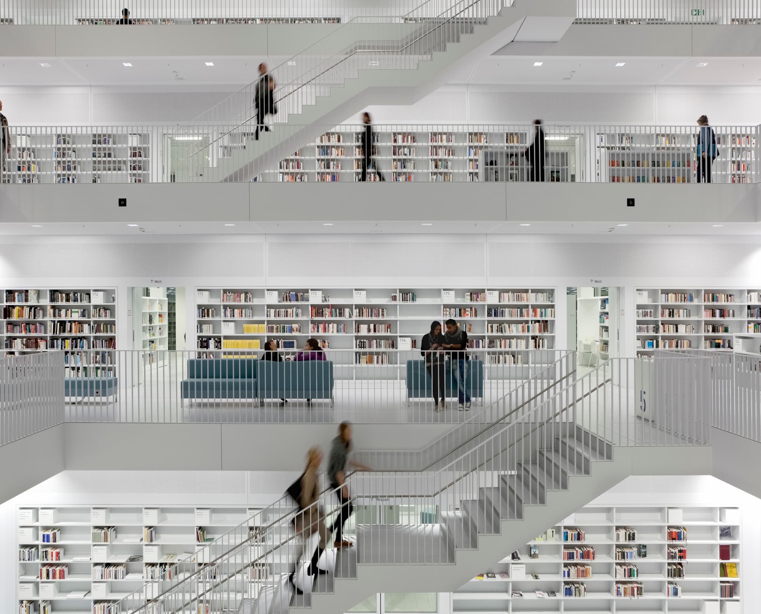 Innenansicht einer Bibliothek mit mehreren Etagen, Treppen und Regalen voller Bücher, beleuchtet mit ERCO Licht.