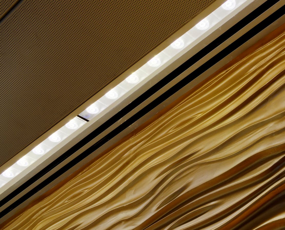ERCO Wandfluter beleuchten eine goldene Wand unter einer Decke, die eine helle und einladende Atmosphäre schafft.
