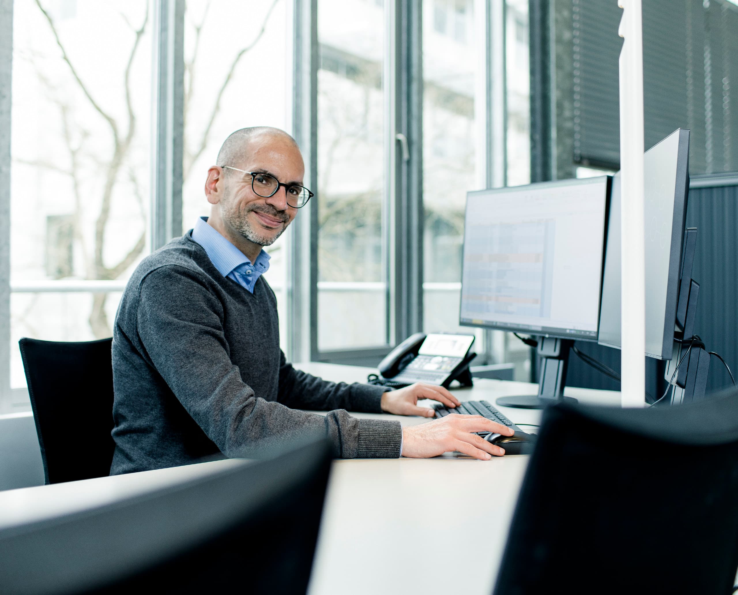 ERCO Vertriebsmitarbeiter bei der Arbeit am Computer im Büro, Fokussiert auf Lichtplanung.