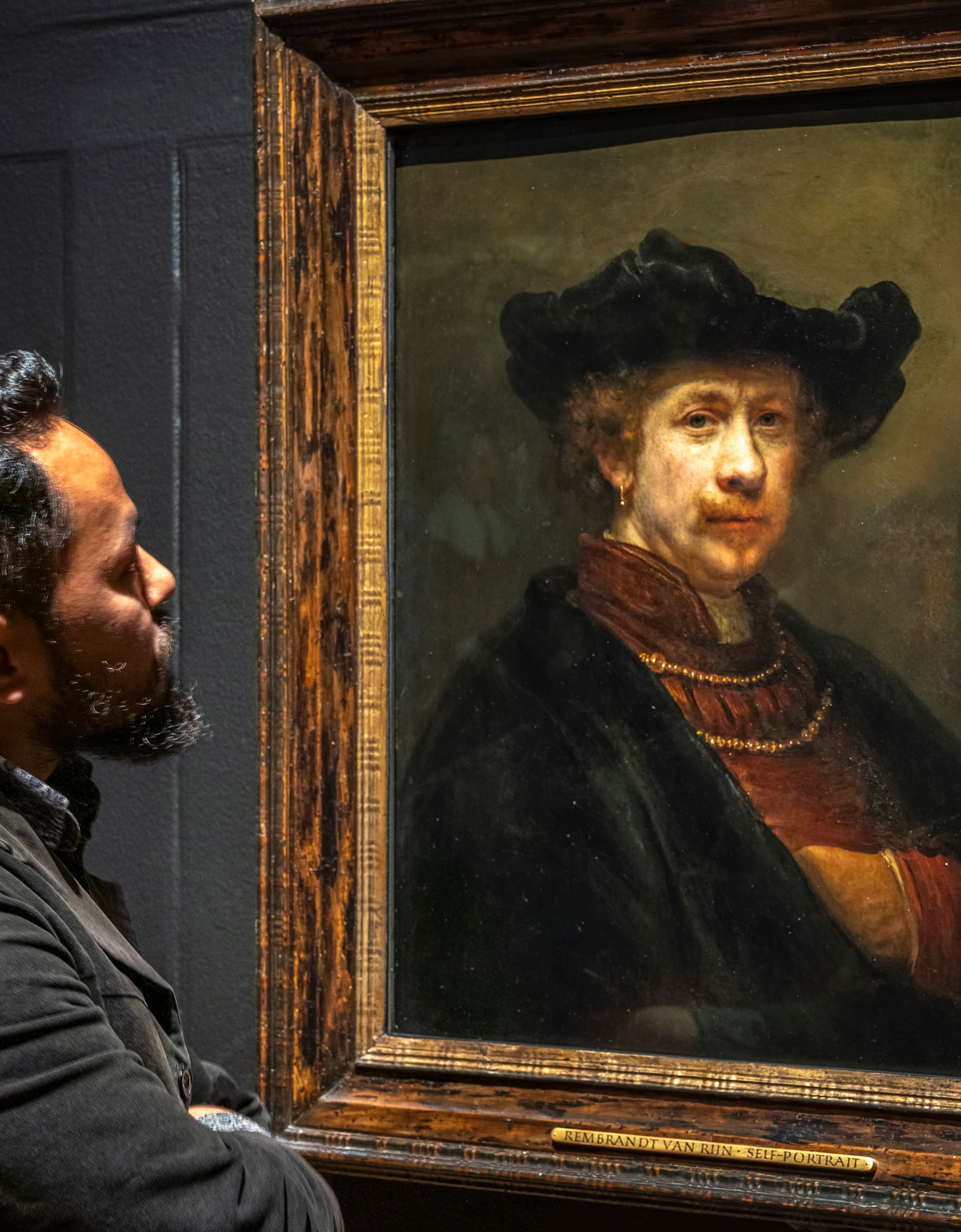 Ein Mann betrachtet ein Gemälde von Rembrandt, wobei die Lichtgestaltung die Wahrnehmung beeinflusst.