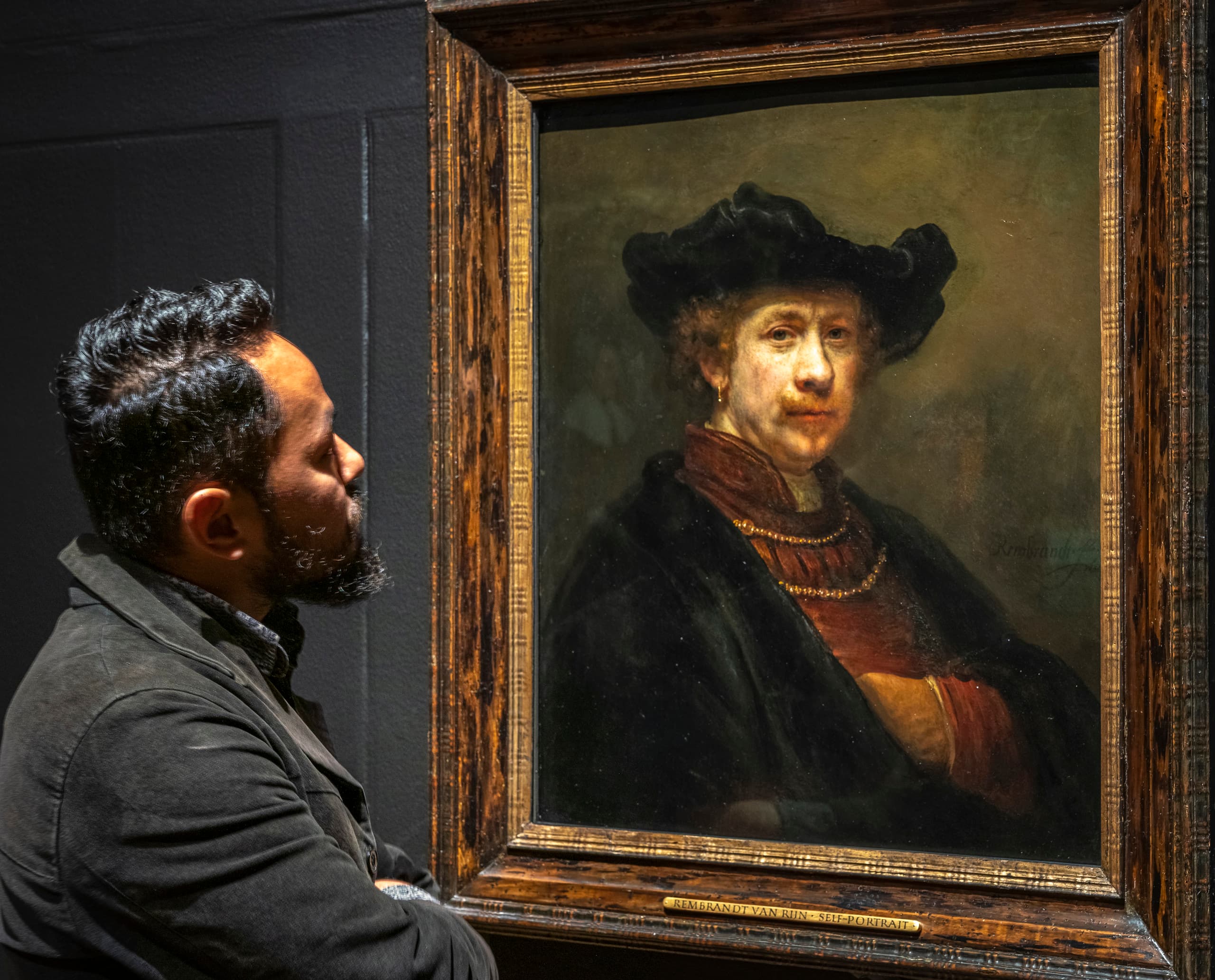 Ein Mann betrachtet ein Gemälde von Rembrandt, wobei die Lichtgestaltung die Wahrnehmung beeinflusst.