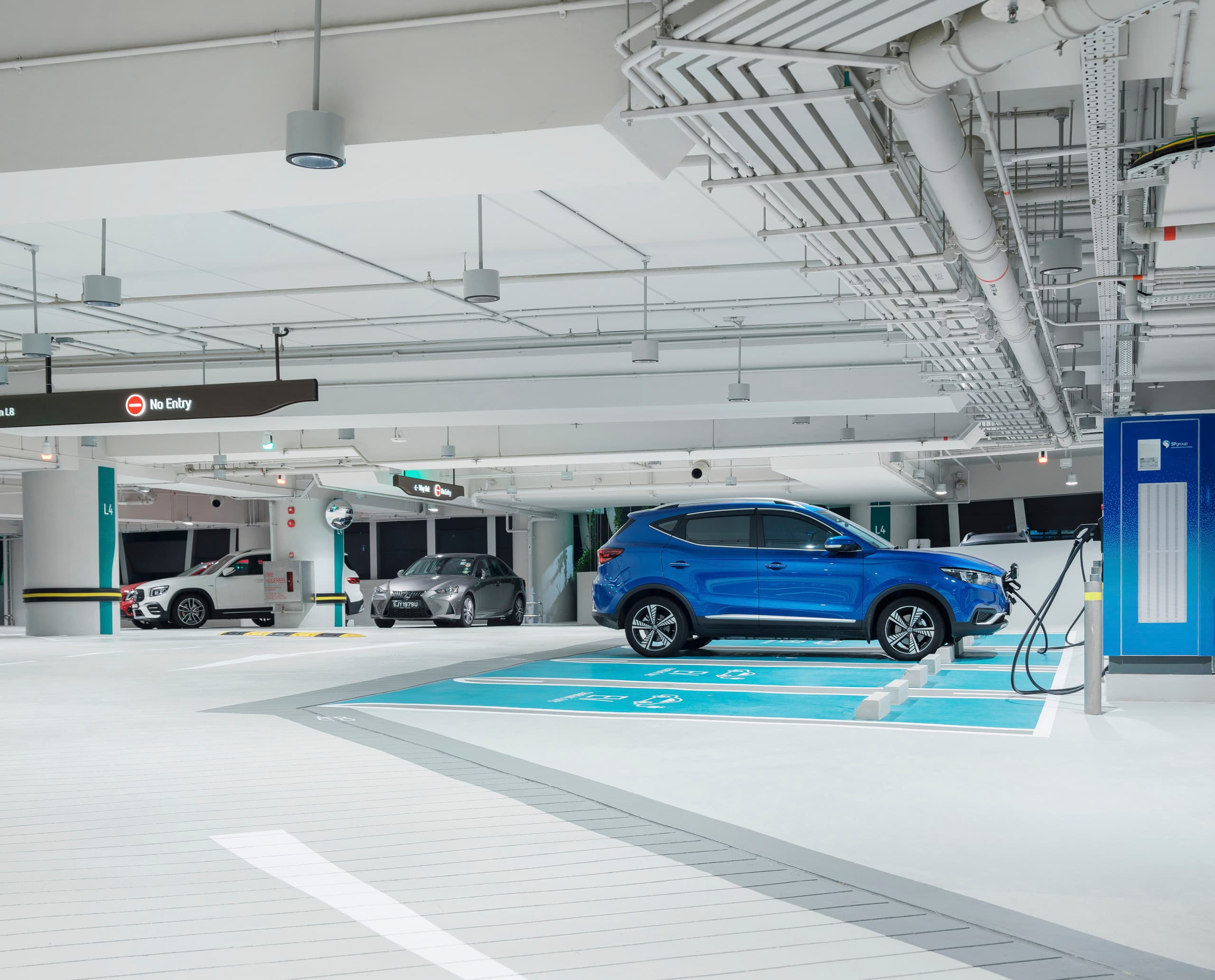 ERCO Beleuchtung im CapitaSpring Parkhaus, Singapur, mit Elektroauto an Ladestation und Skim Downlights für blendfreie, visuelle Sicherheit.