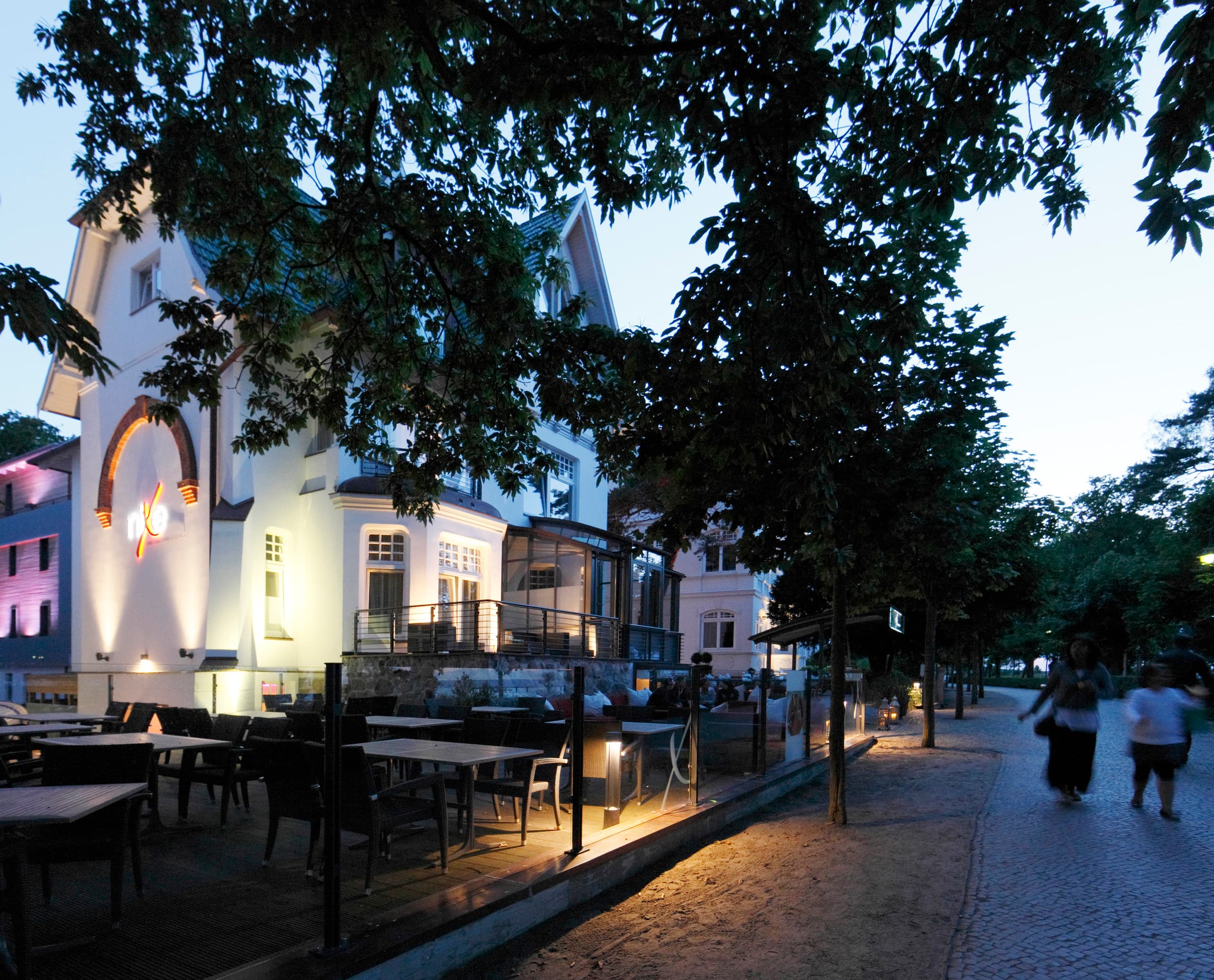 Beleuchtetes Hotel Nixe in Binz mit Midipoll-Leuchten auf der Terrasse und Fassadenstrahlern.