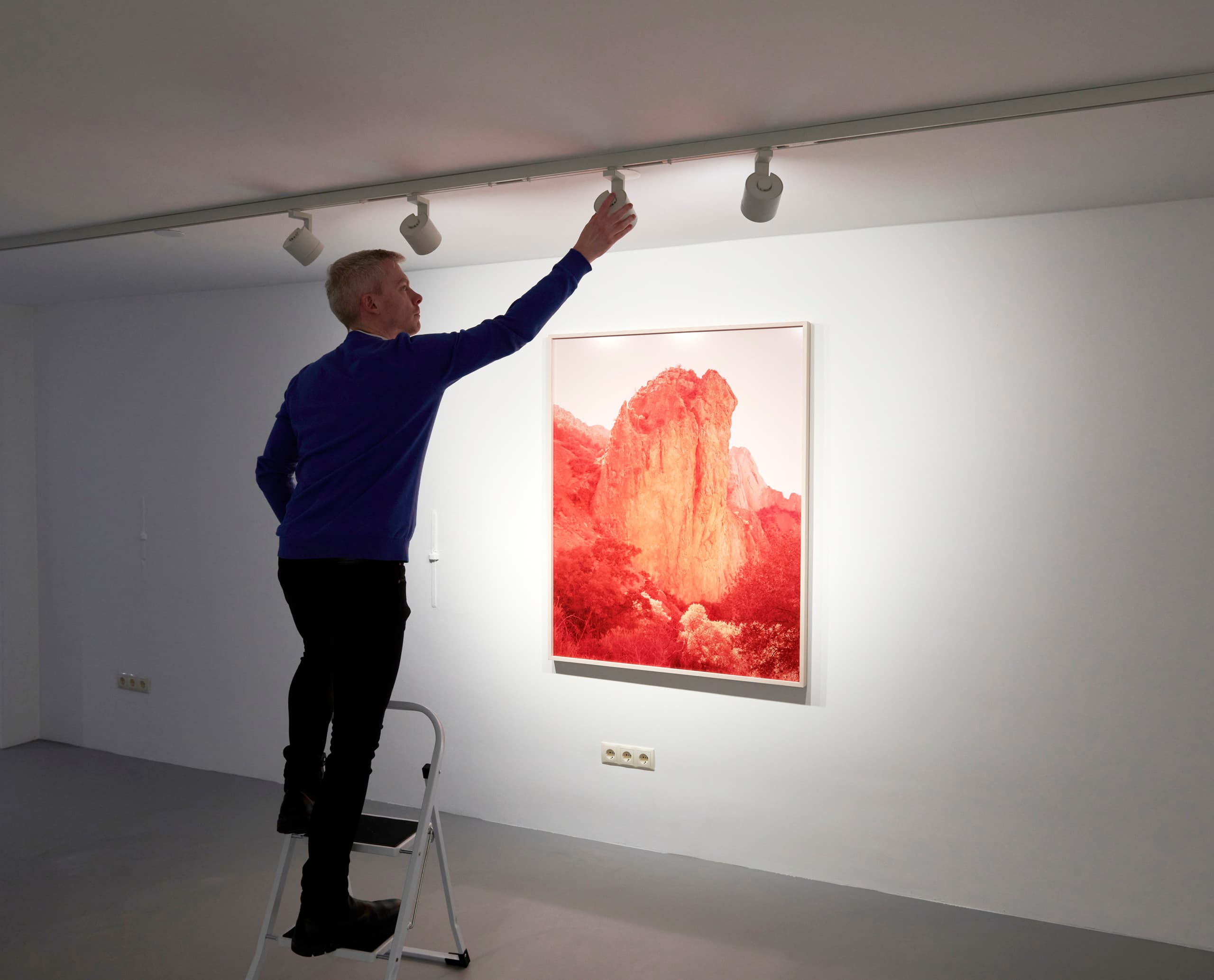 Ein Mann justiert einen ERCO Parscan InTrack Strahler in der Enari Galerie, um ein Kunstwerk optimal zu beleuchten.