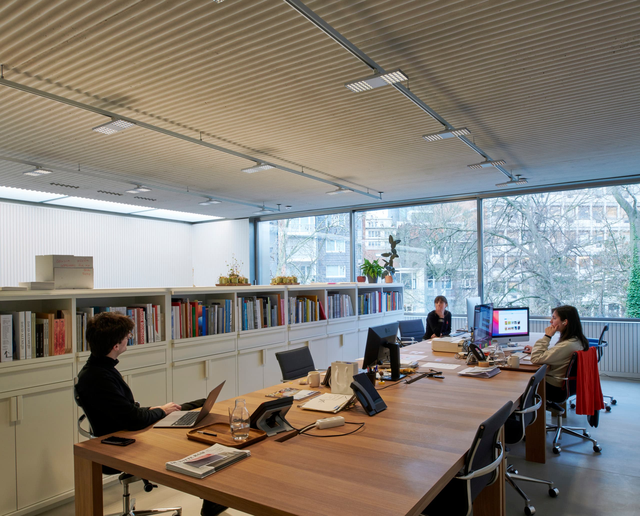 ERCO Jilly Downlights beleuchten einen Büroraum mit Bücherregal und großem Tisch für komfortables Arbeiten.