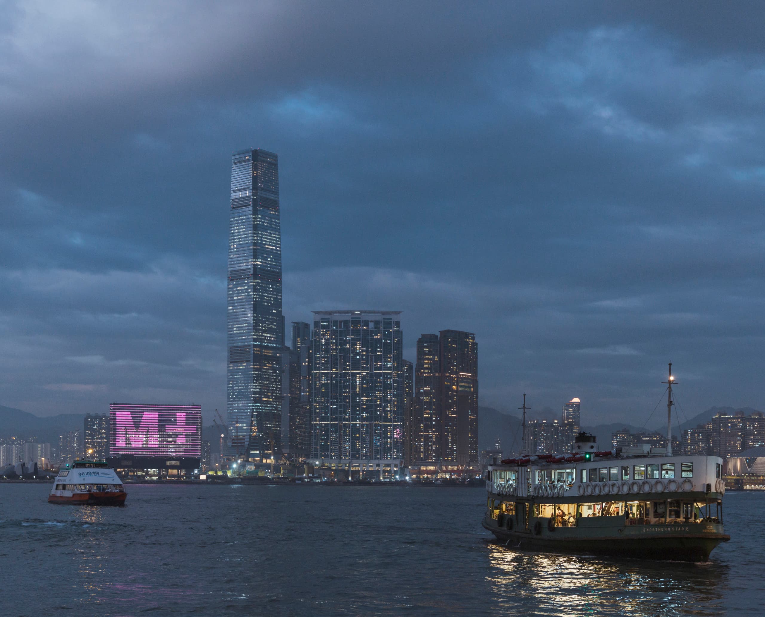 Die beleuchtete Fassade des M+ Museums in Hongkong, gesehen vom Hafen aus.